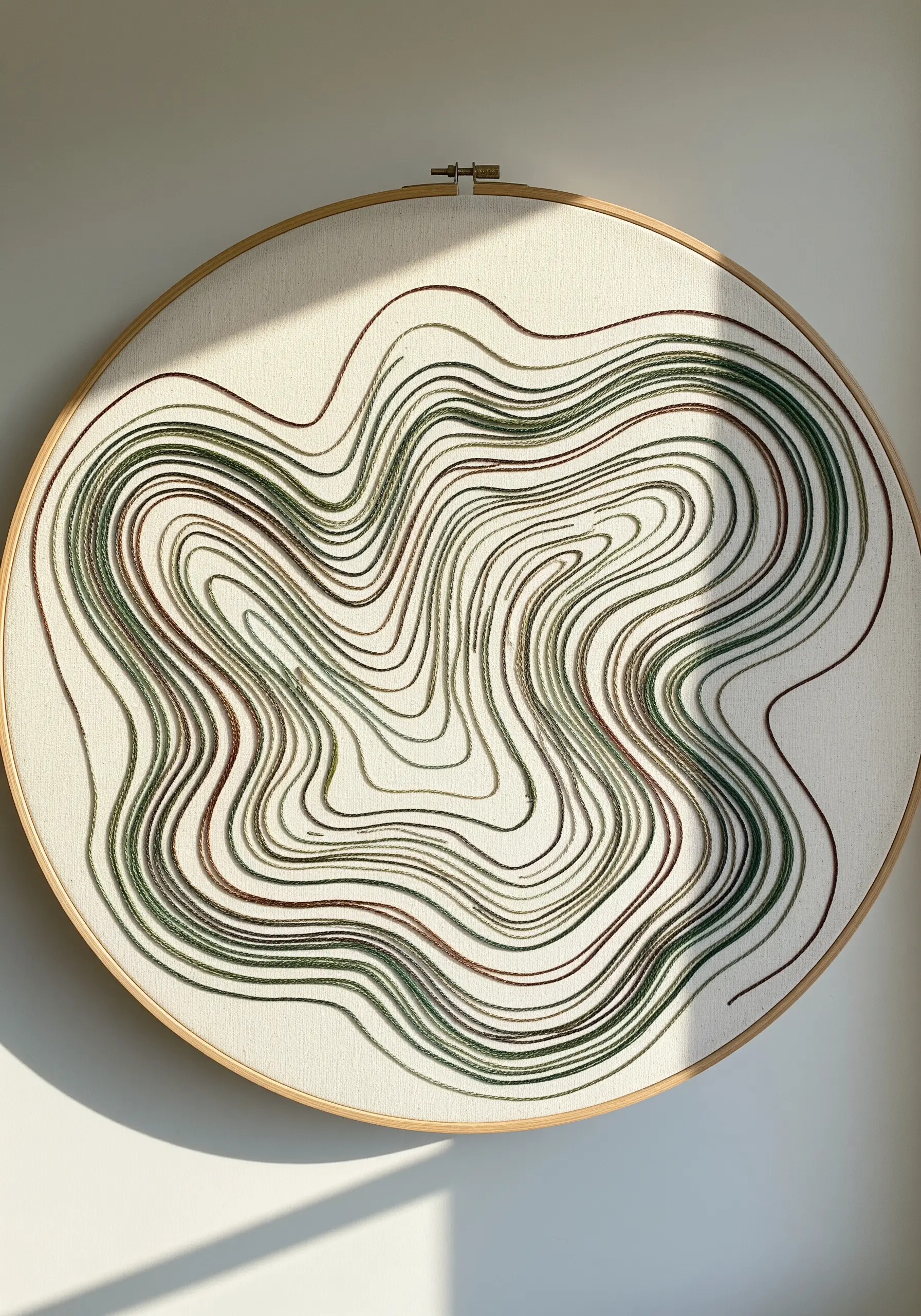 Flowing, concentric lines in variegated green and brown thread resembling a topographic map.