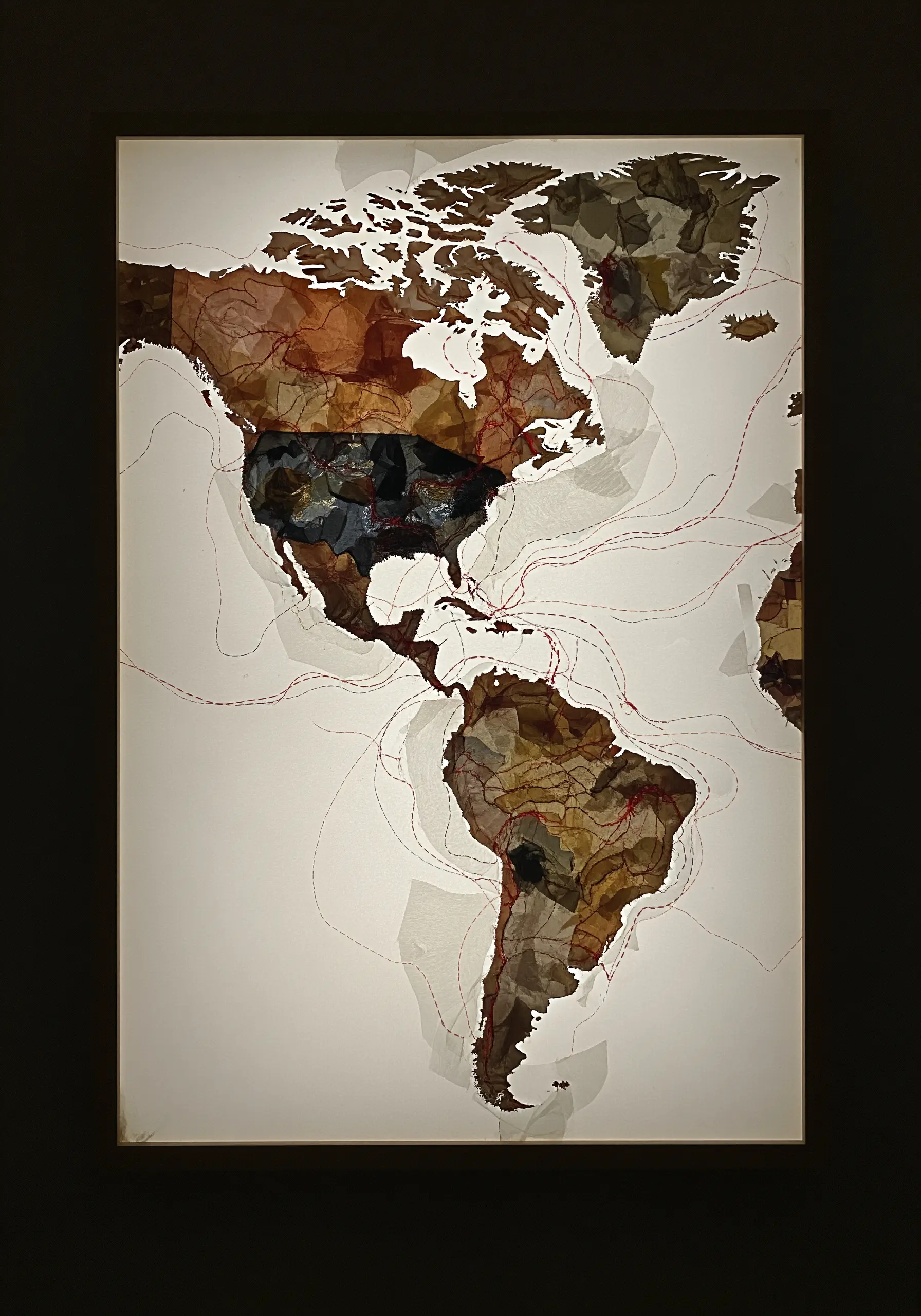 A world map made of earthy-toned fabric scraps with red stitched travel routes.