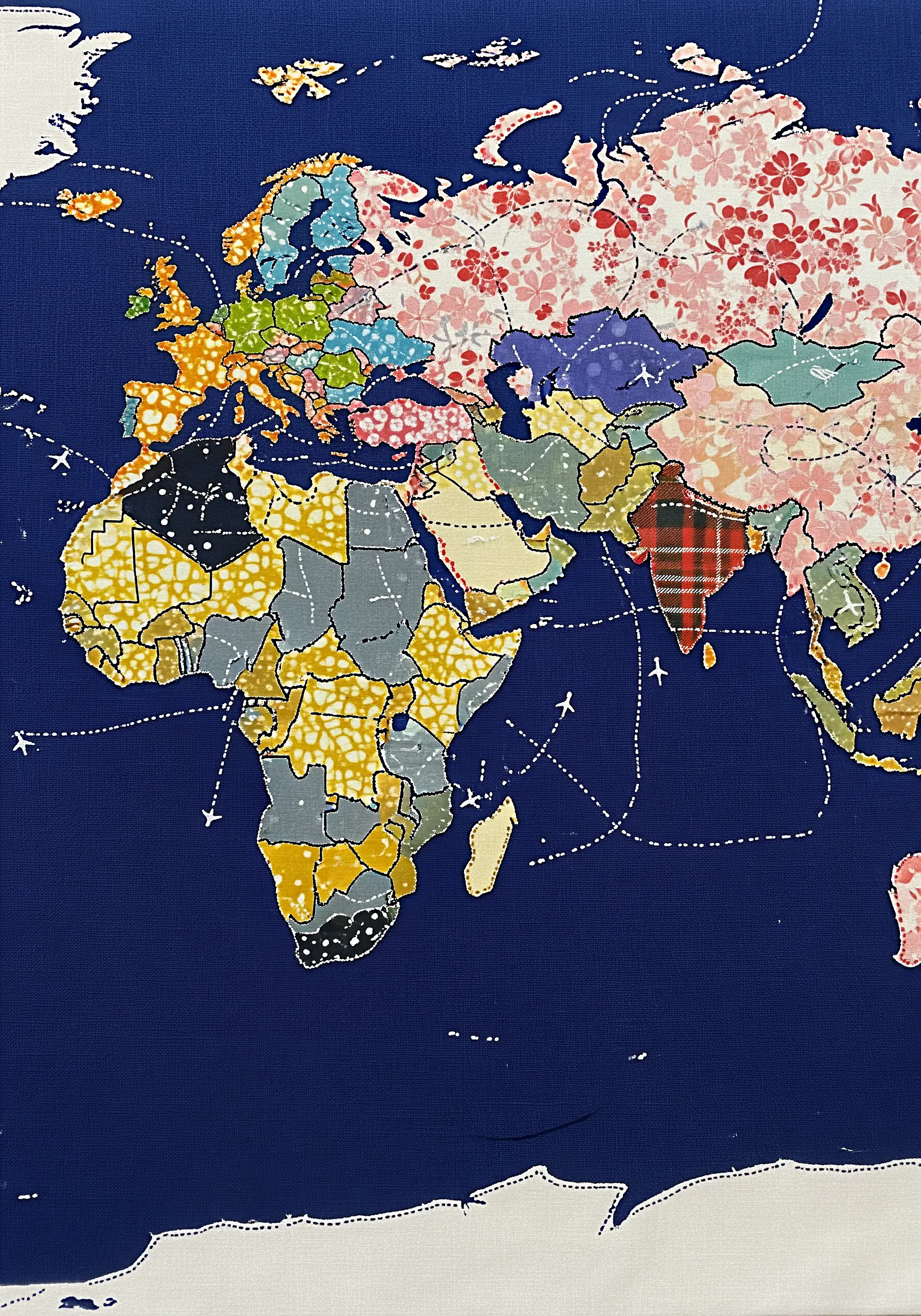 A world map made from colorful, patterned fabric appliqué with stitched travel routes
