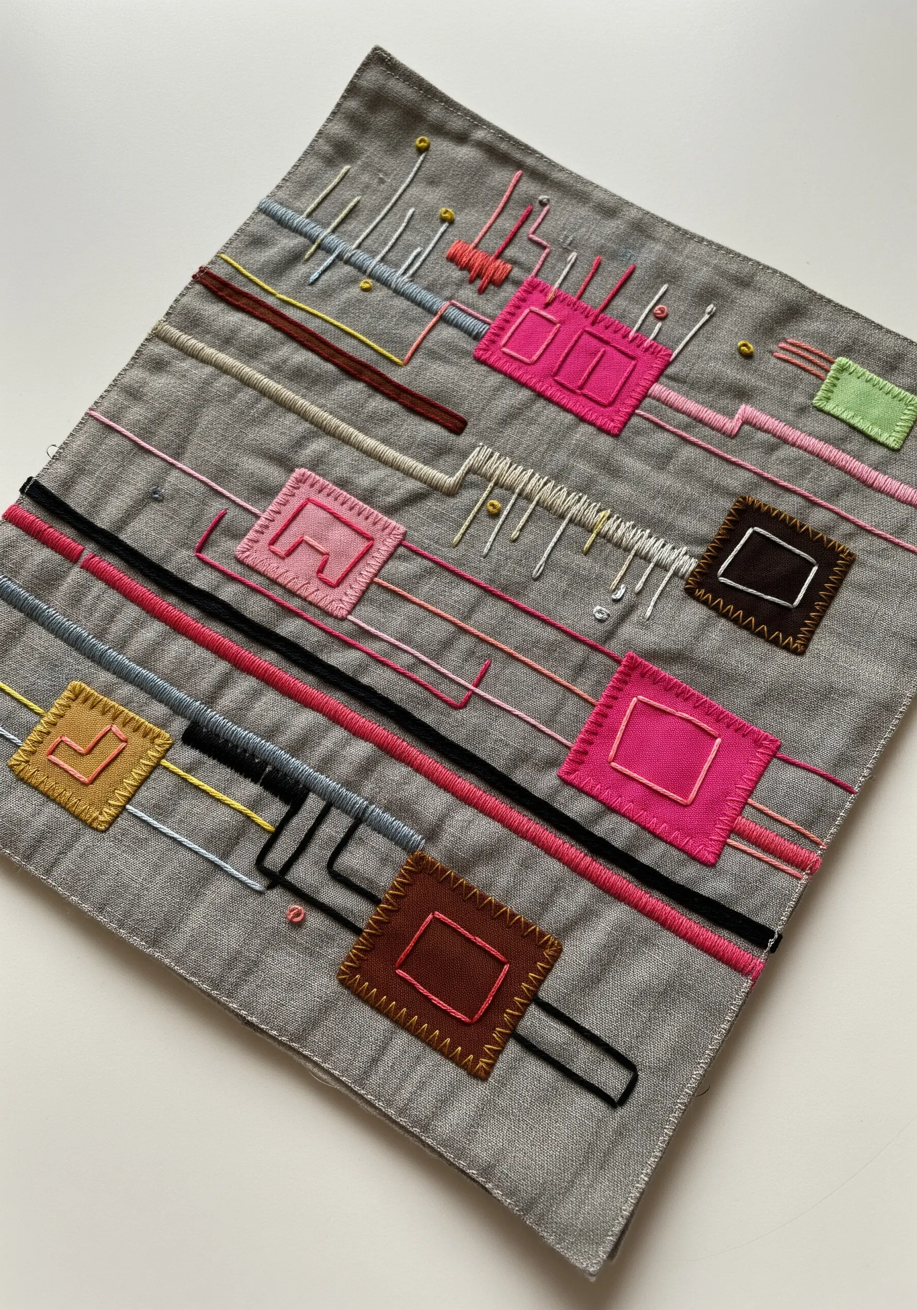 Abstract embroidery with appliquéd fabric squares connected by various straight and couched stitches.