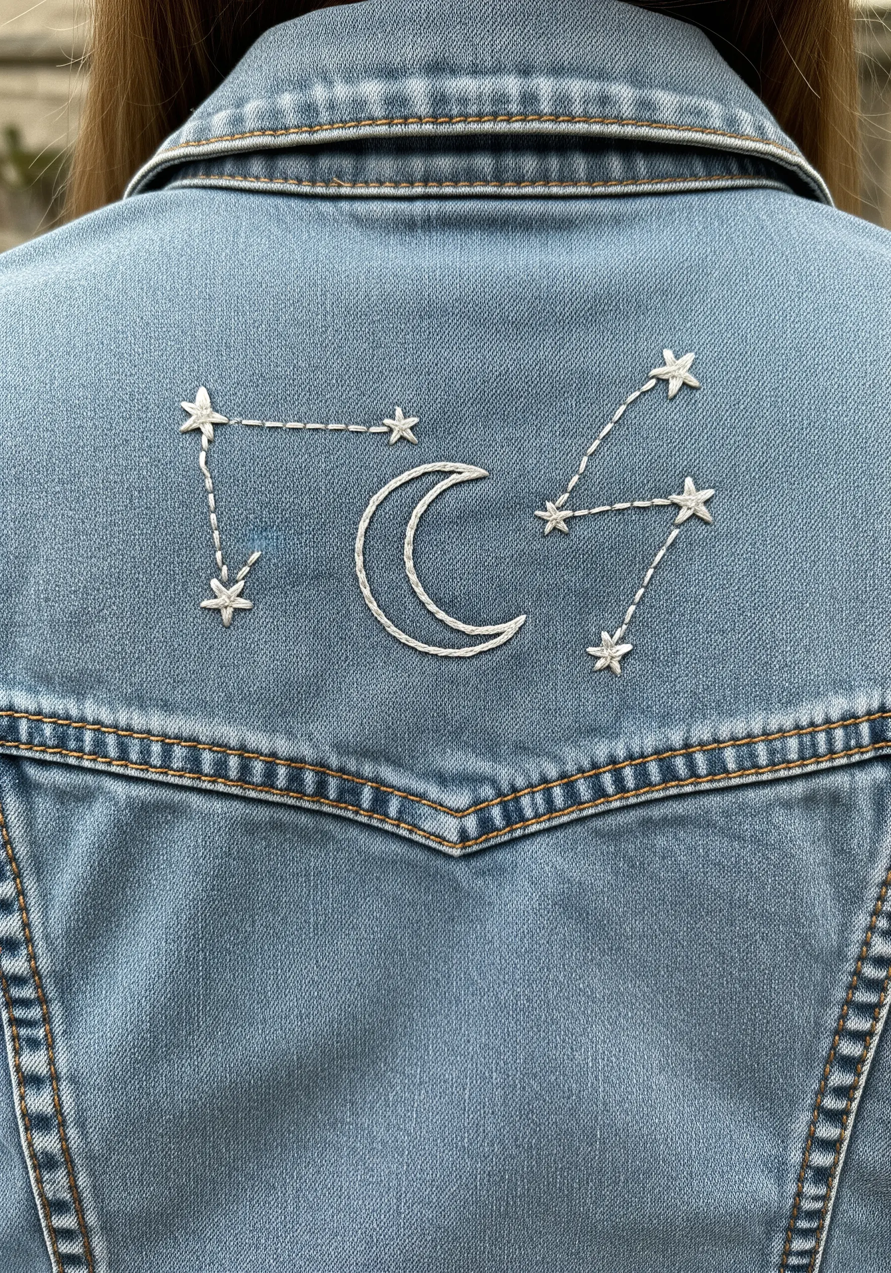 Embroidered constellations with a crescent moon on the back of a light-wash denim jacket.