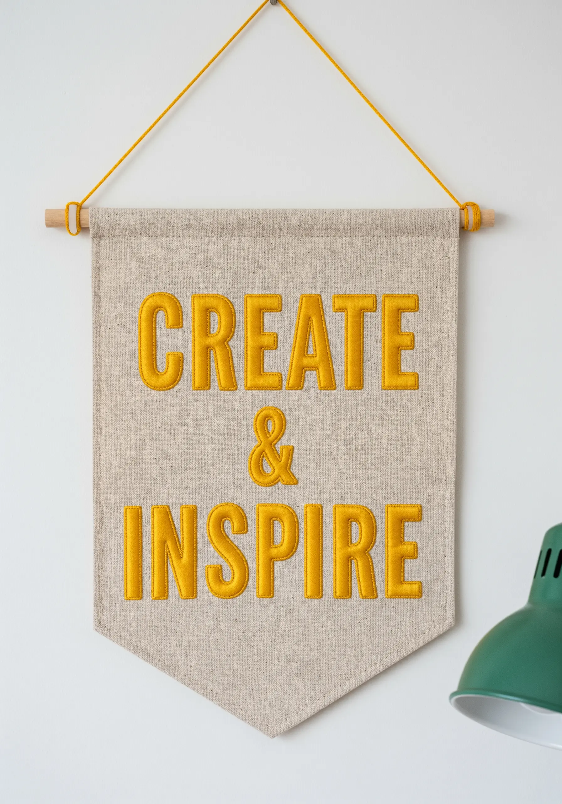 A canvas pennant with the words 'Create & Inspire' stitched in raised yellow satin stitch.