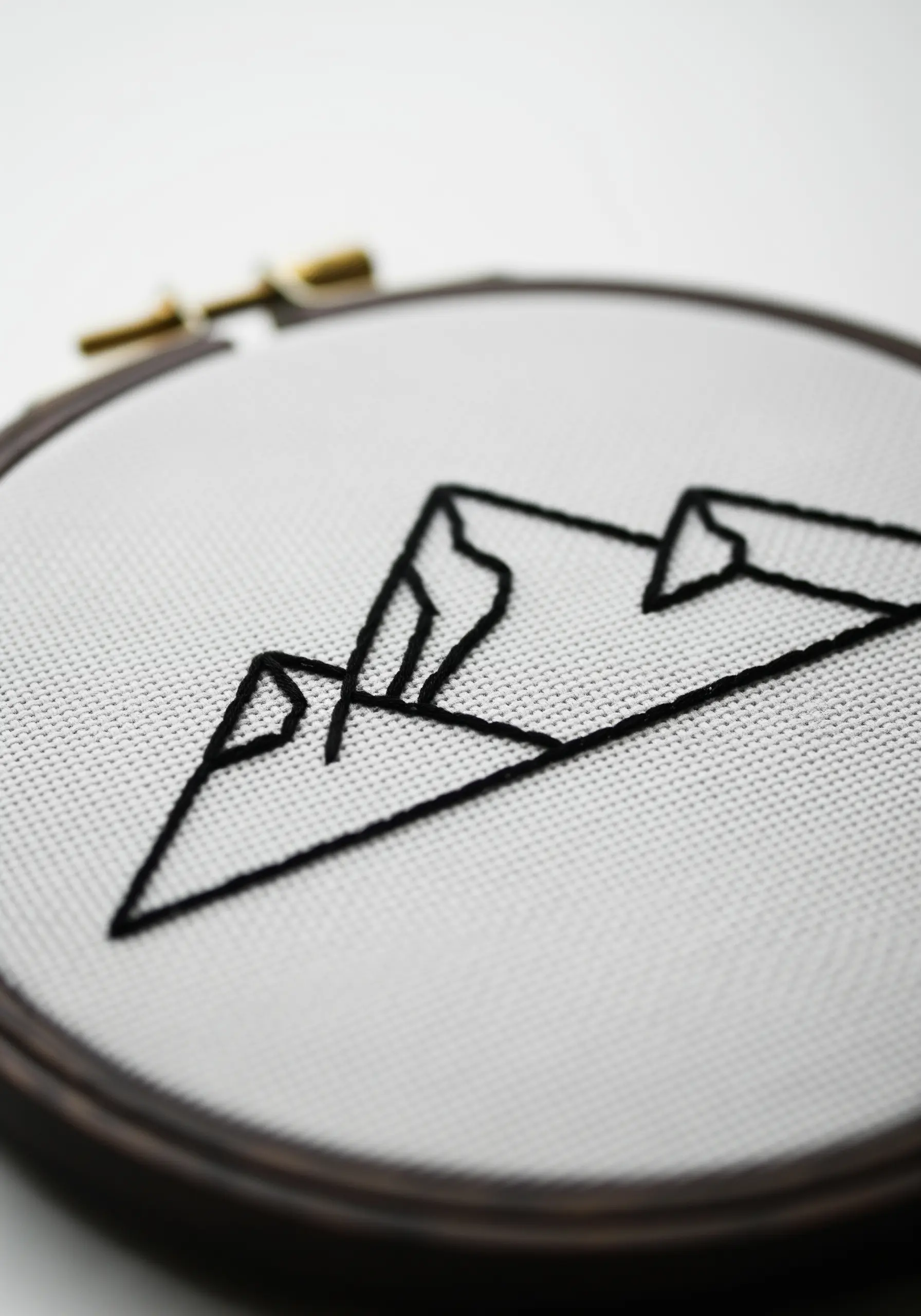 Minimalist black-thread mountain range outline embroidered on white Aida cloth in a dark hoop.