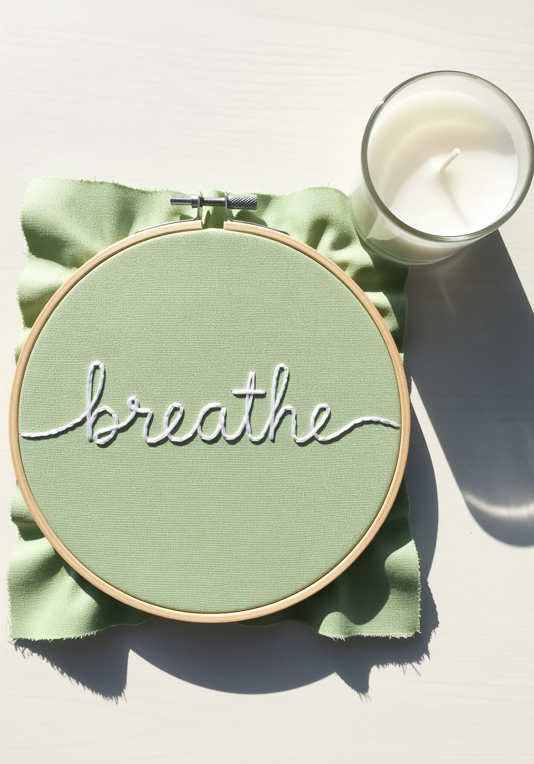 The word 'breathe' embroidered in white cursive script on sage green fabric.