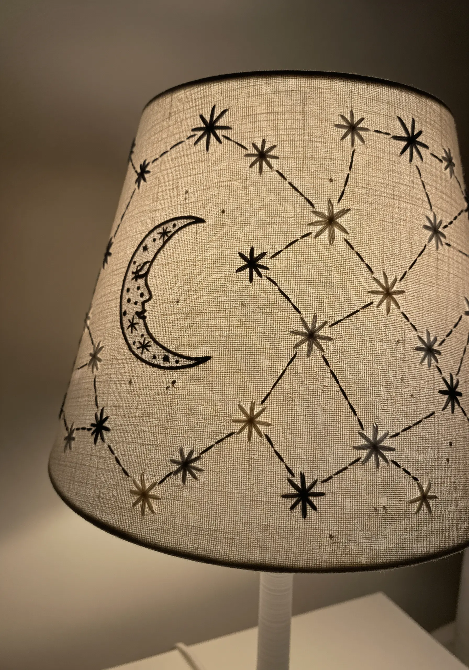 A linen lampshade embroidered with a celestial pattern of stars and a crescent moon.