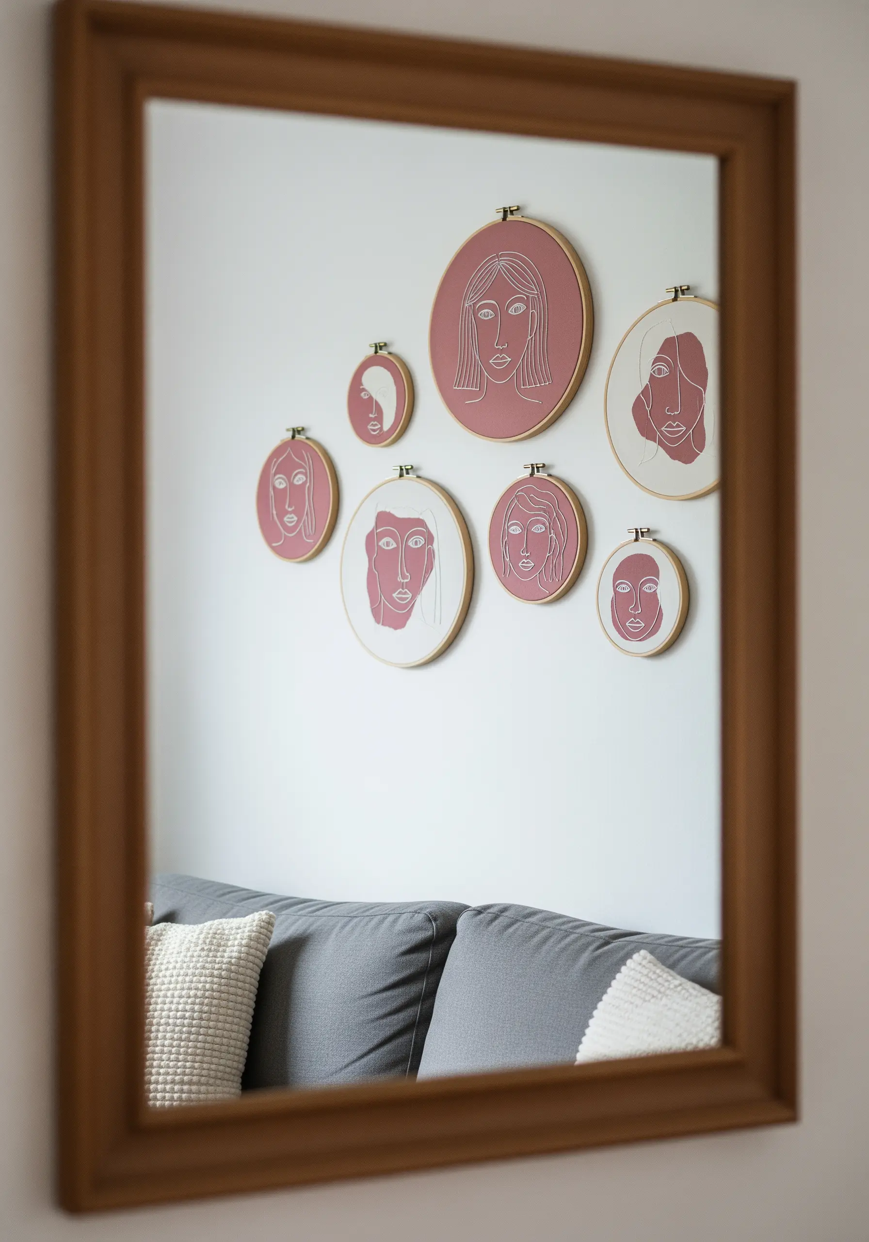 A gallery wall of minimalist line-art portraits embroidered in ivory on dusty rose fabric.