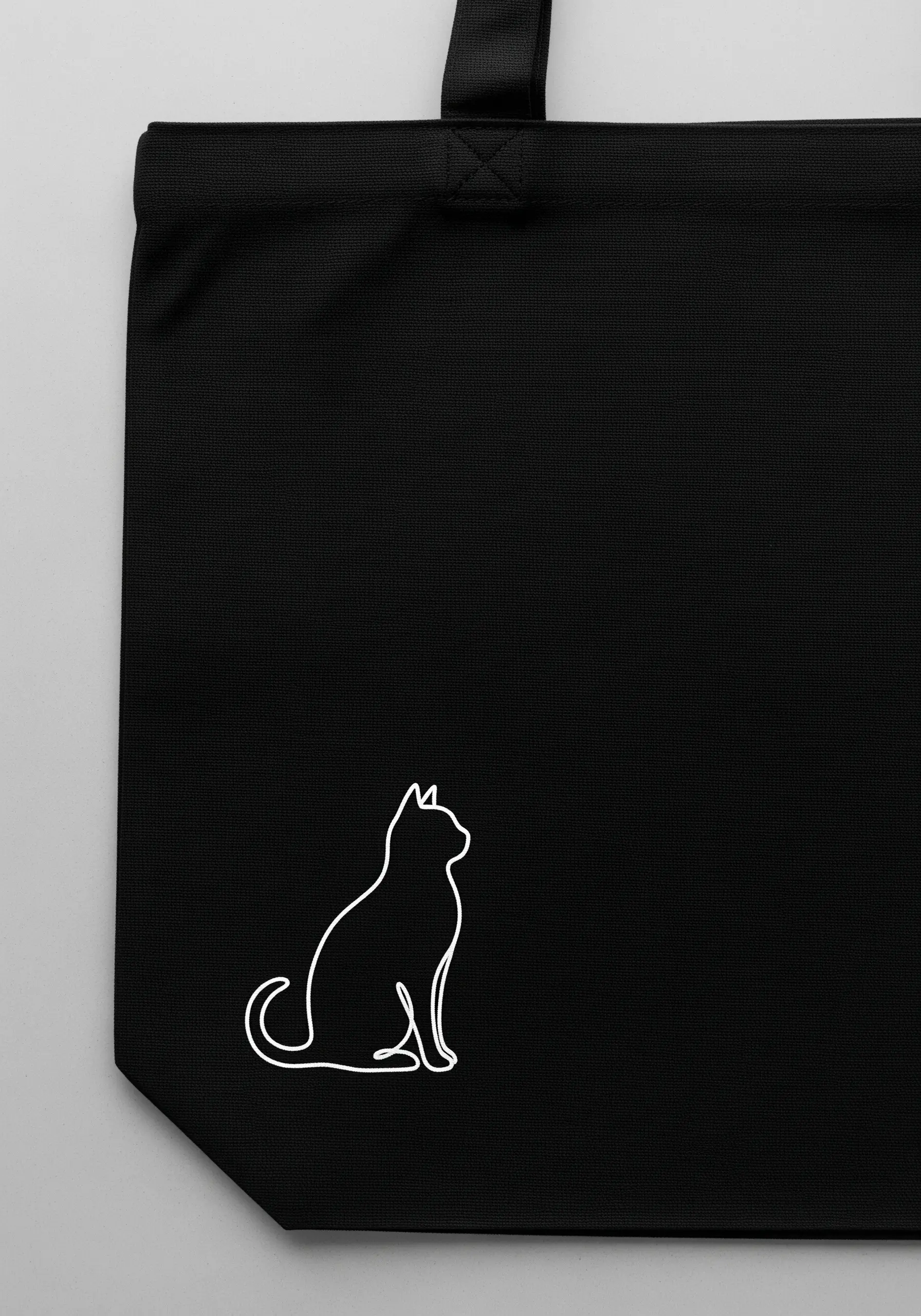 A continuous single-line art drawing of a sitting cat stitched in white on a black tote bag.