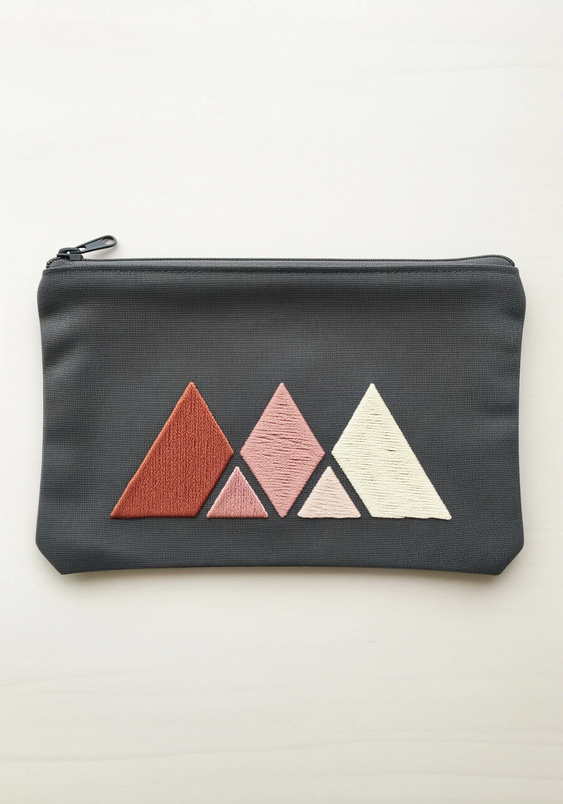 Four geometric triangles filled with satin stitch in shades of pink and cream on a pouch.