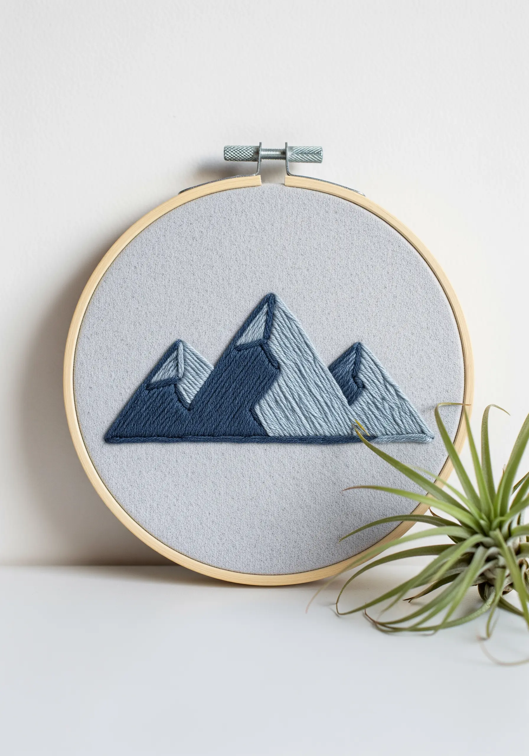 Geometric mountain range in shades of blue, filled with smooth satin stitch on gray fabric.