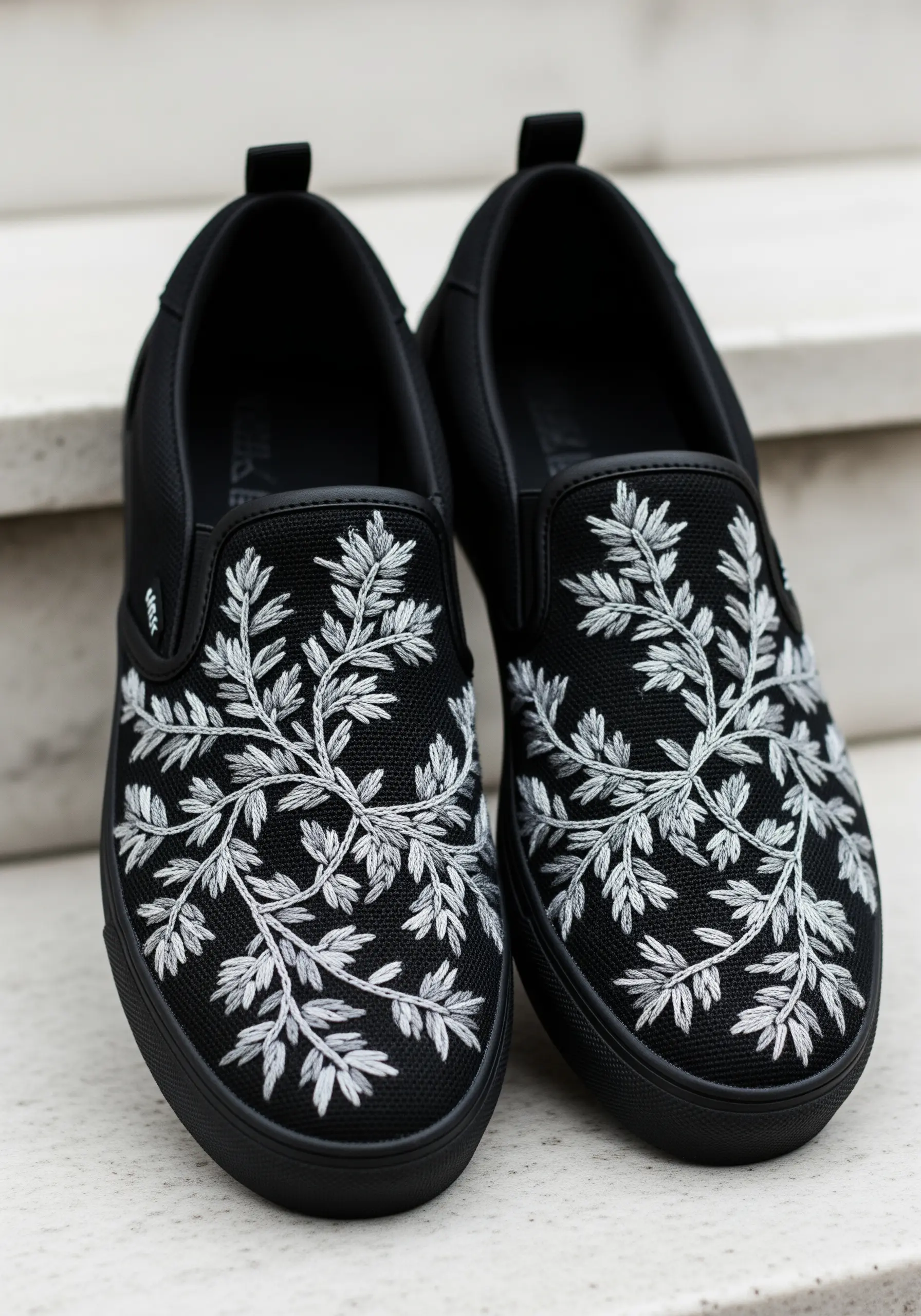 Delicate white foliage embroidered across the top of black slip-on canvas sneakers.