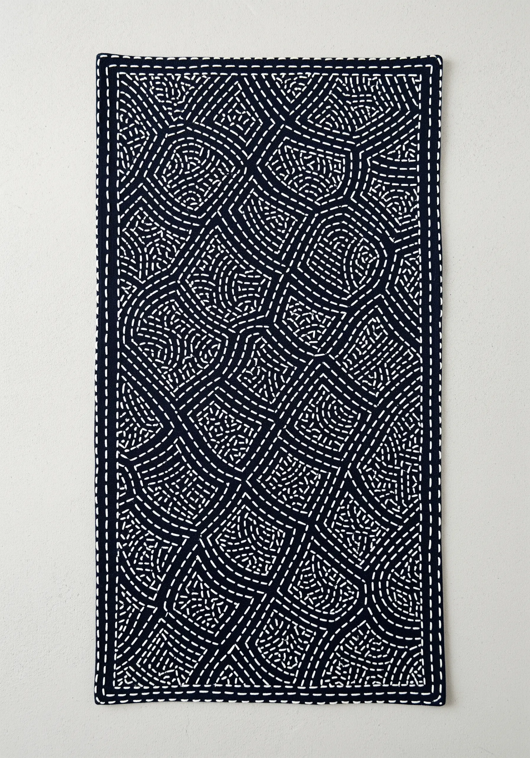 A traditional Japanese Sashiko pattern in white thread on a dark indigo table runner.