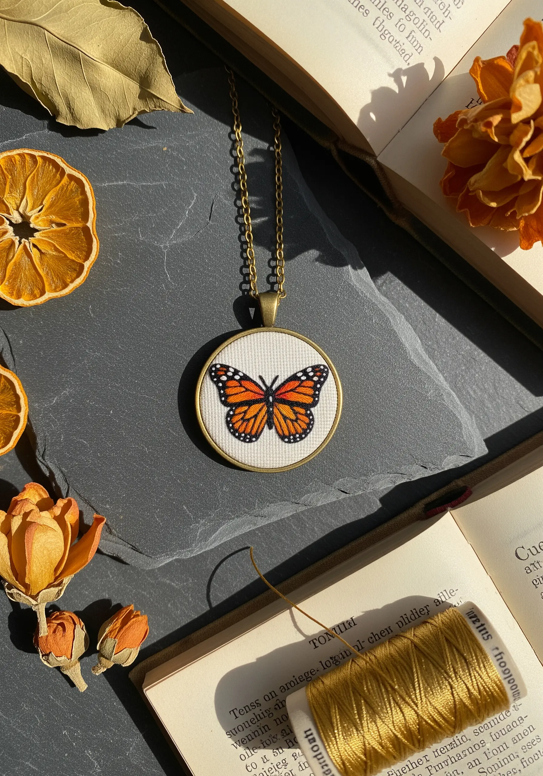 A small embroidered monarch butterfly pendant necklace on a slate background