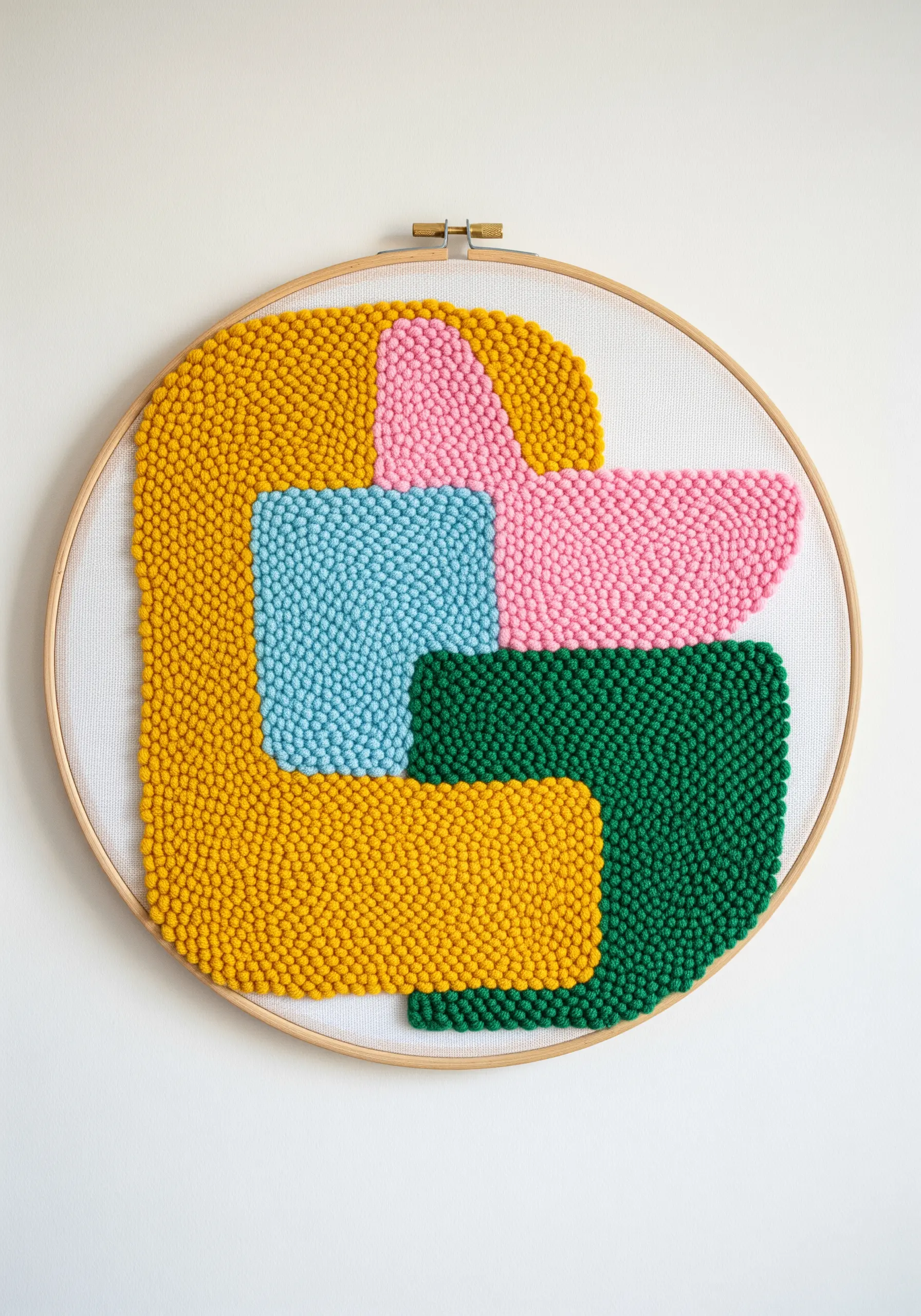 A punch needle hoop art piece with bold, interlocking abstract shapes in yellow, pink, blue, and green.