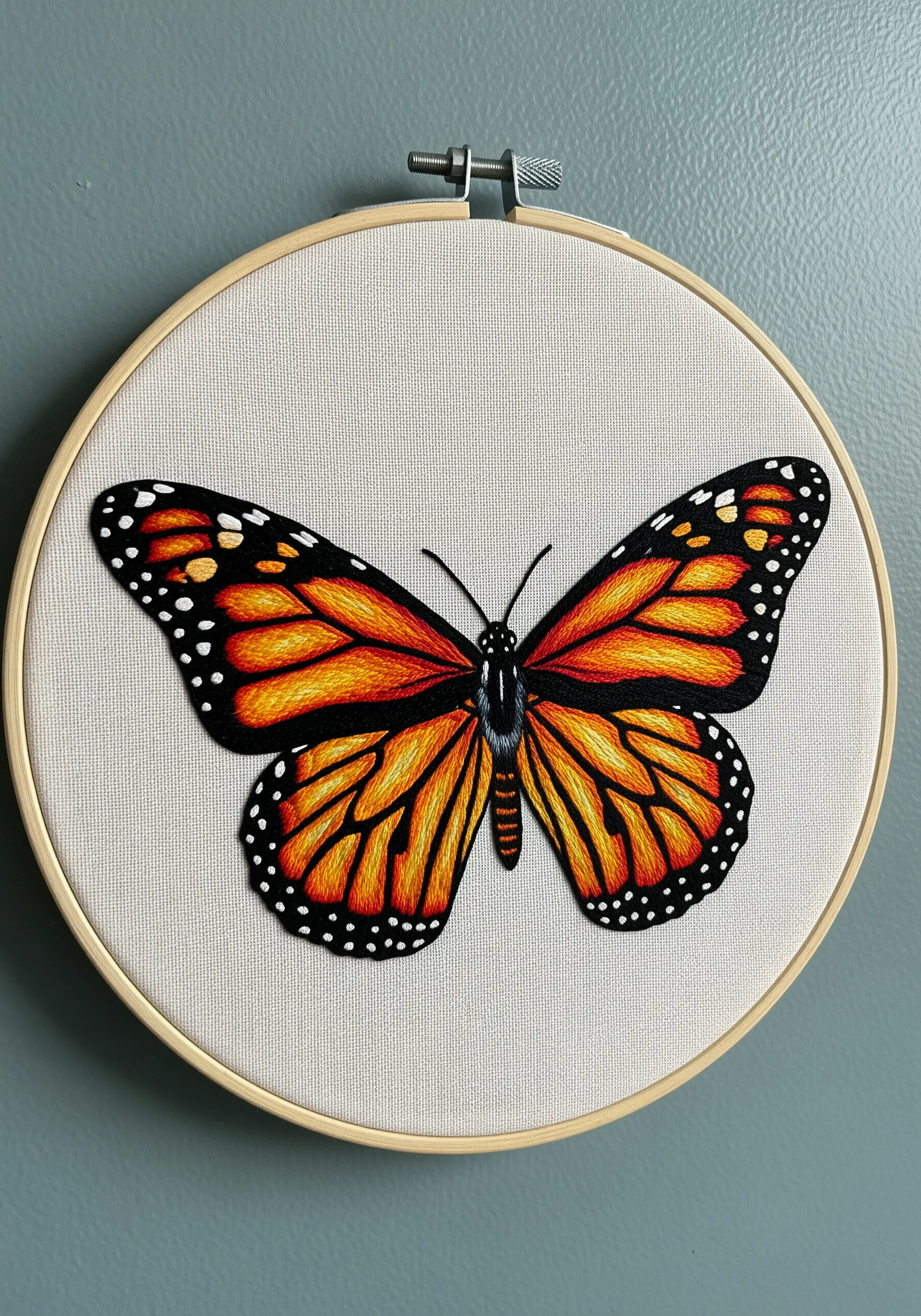 A highly detailed, thread-painted monarch butterfly on off-white fabric in a wooden hoop.