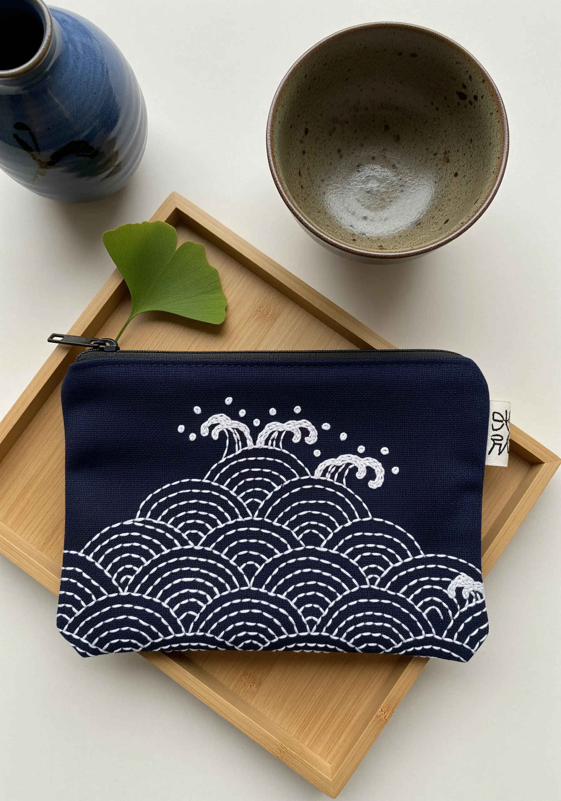 A navy blue pouch with a Japanese-style wave pattern stitched in white thread.