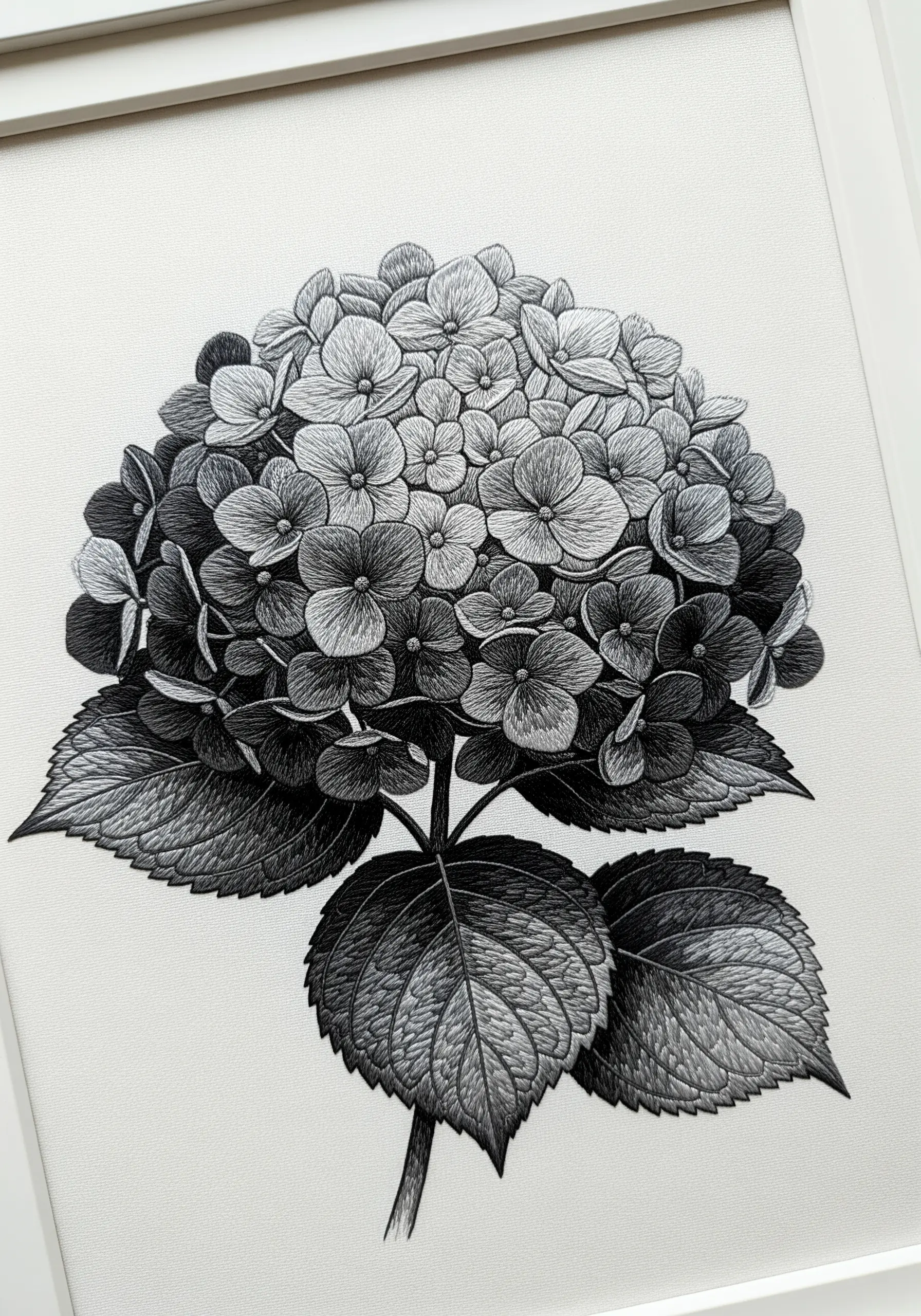 A framed hydrangea embroidered entirely in shades of black, white, and grey.