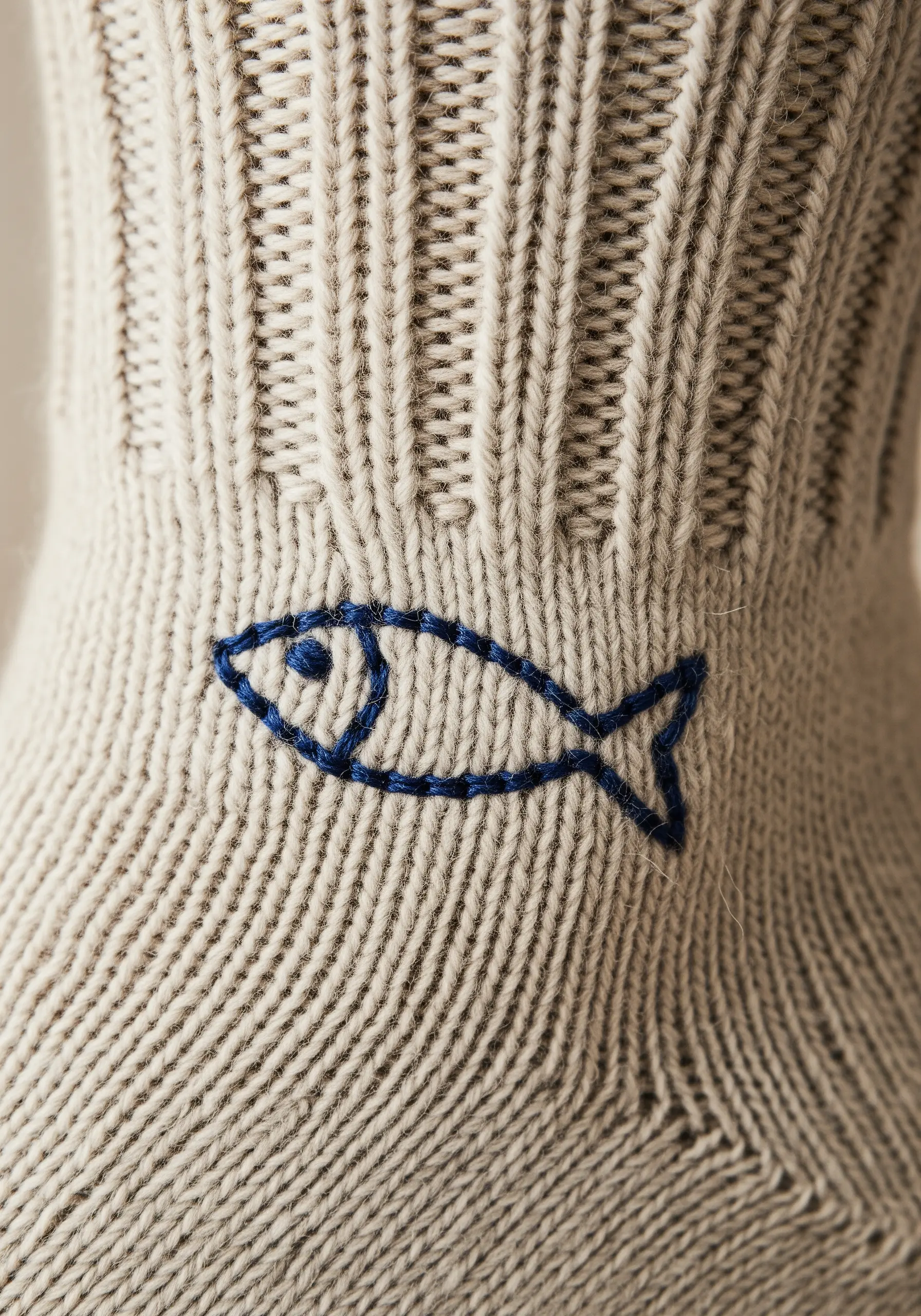 A simple blue backstitch fish outline embroidered on the ankle of a ribbed sock.