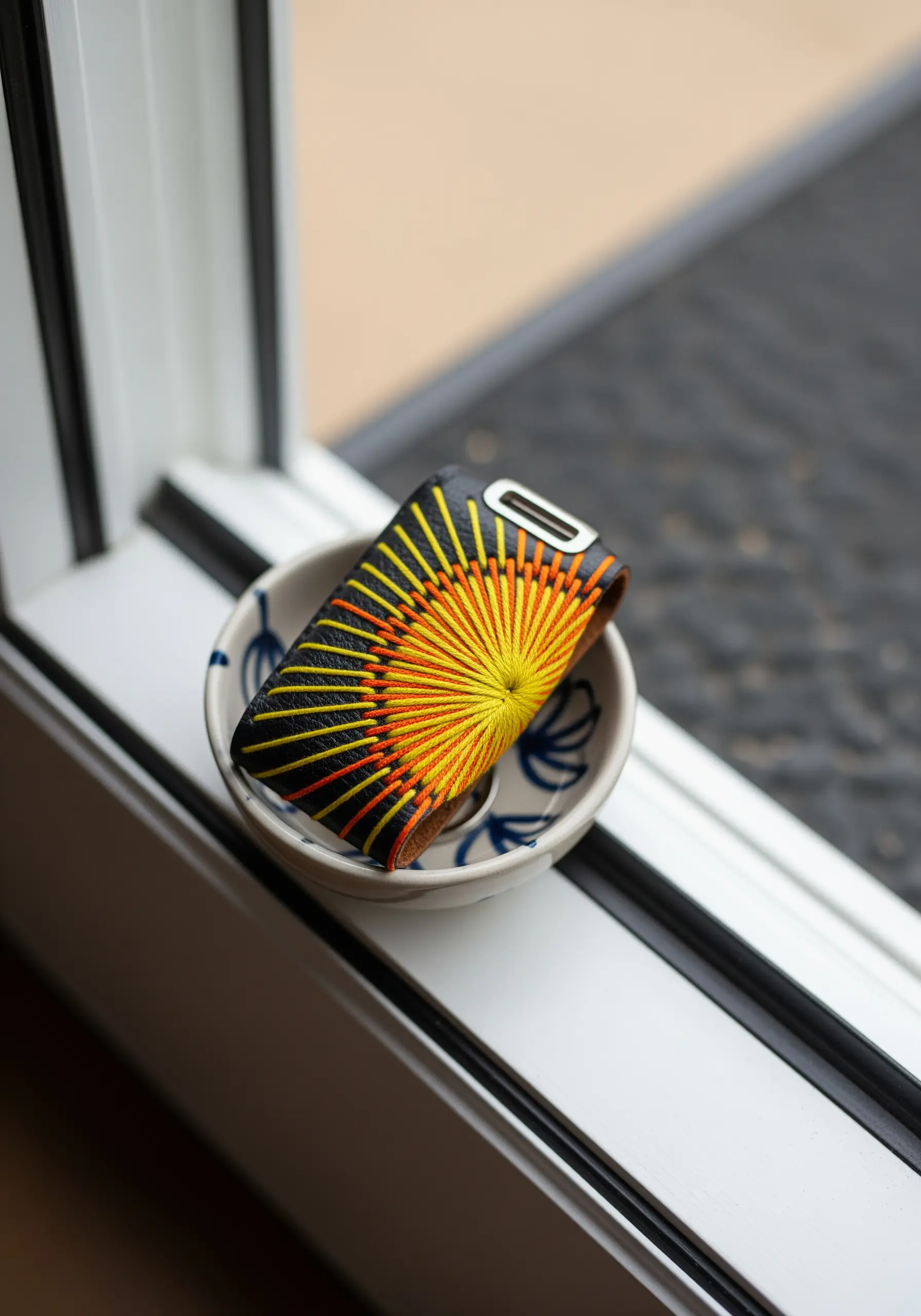 A small leather case decorated with a radiating sunburst pattern in yellow and orange thread.
