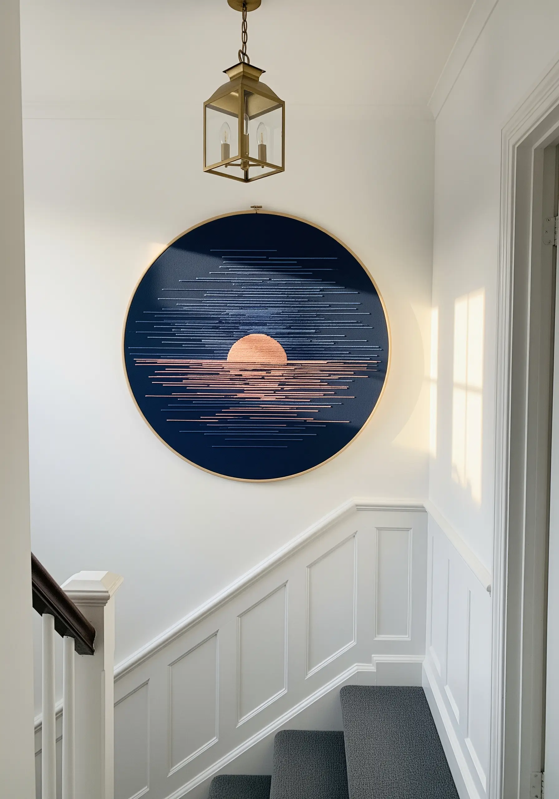 A large embroidery hoop with horizontal lines of thread creating an abstract sunset over water.