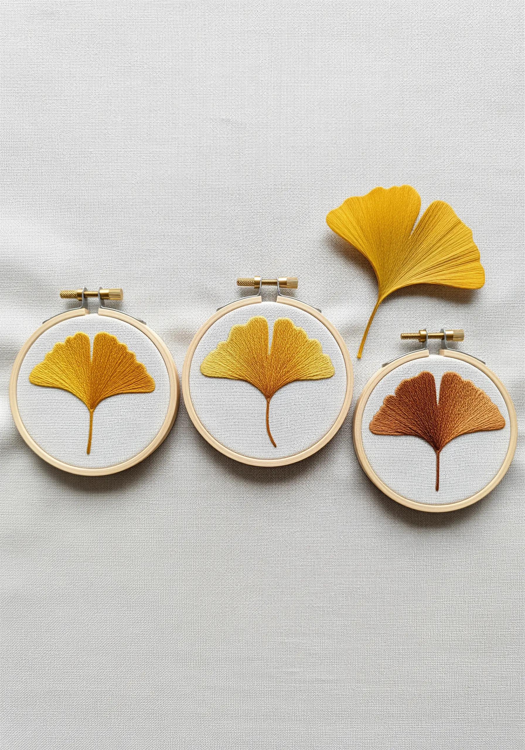 Three embroidery hoops showing ginkgo leaves stitched in a smooth yellow-to-brown gradient.