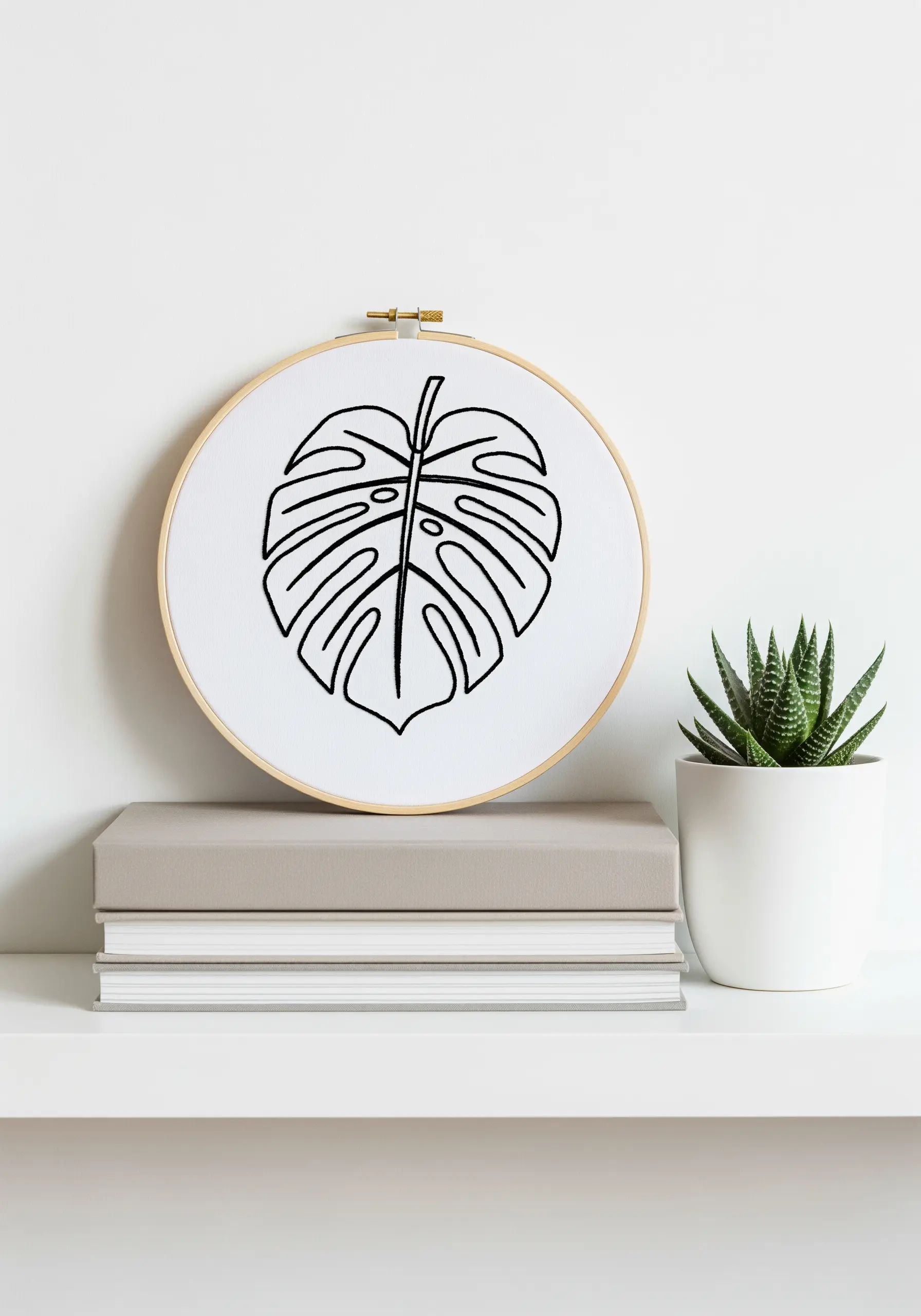 Minimalist black line art embroidery of a Monstera leaf on white fabric in a hoop.