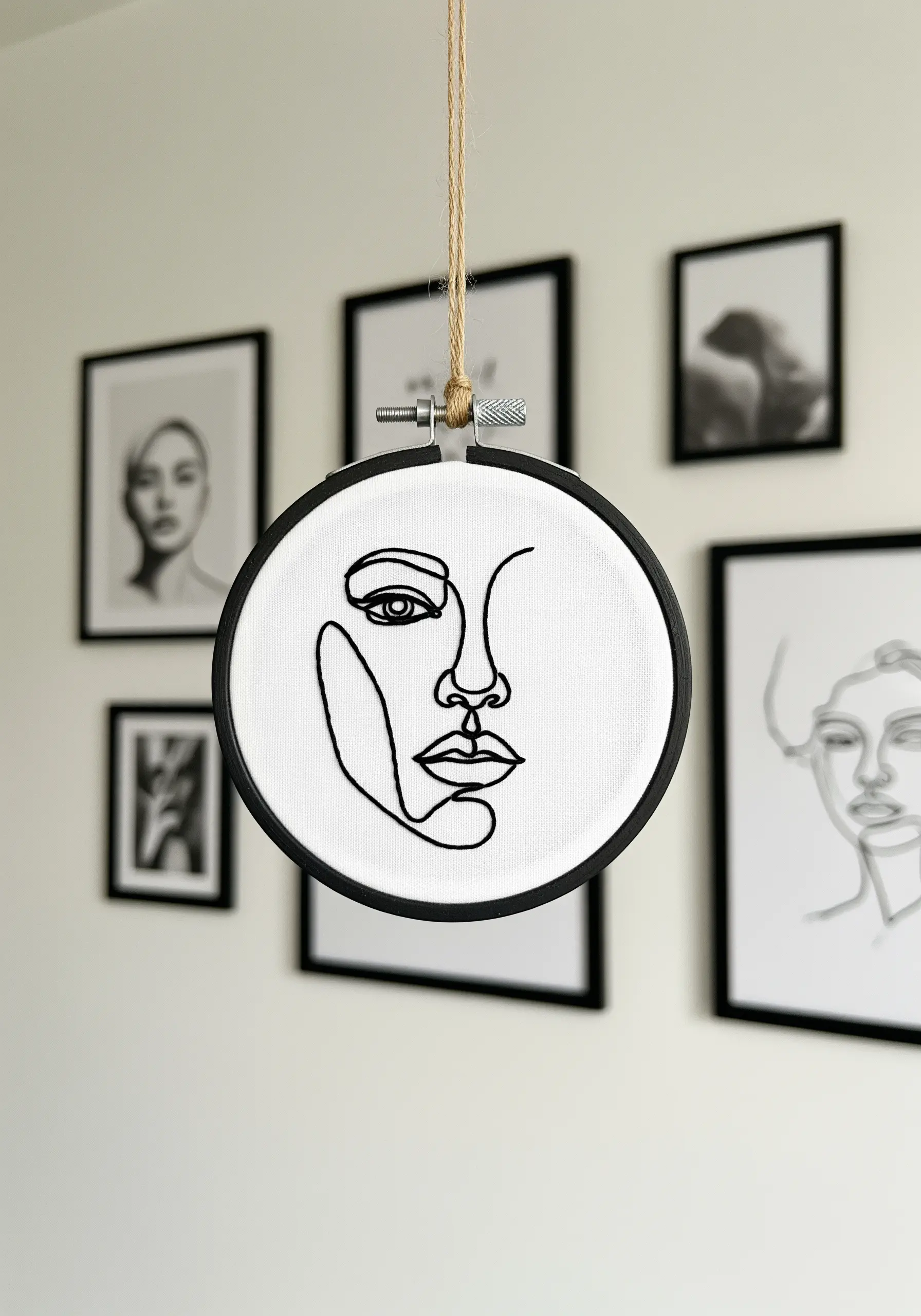 Minimalist single-line face portrait embroidered in black thread on white fabric.