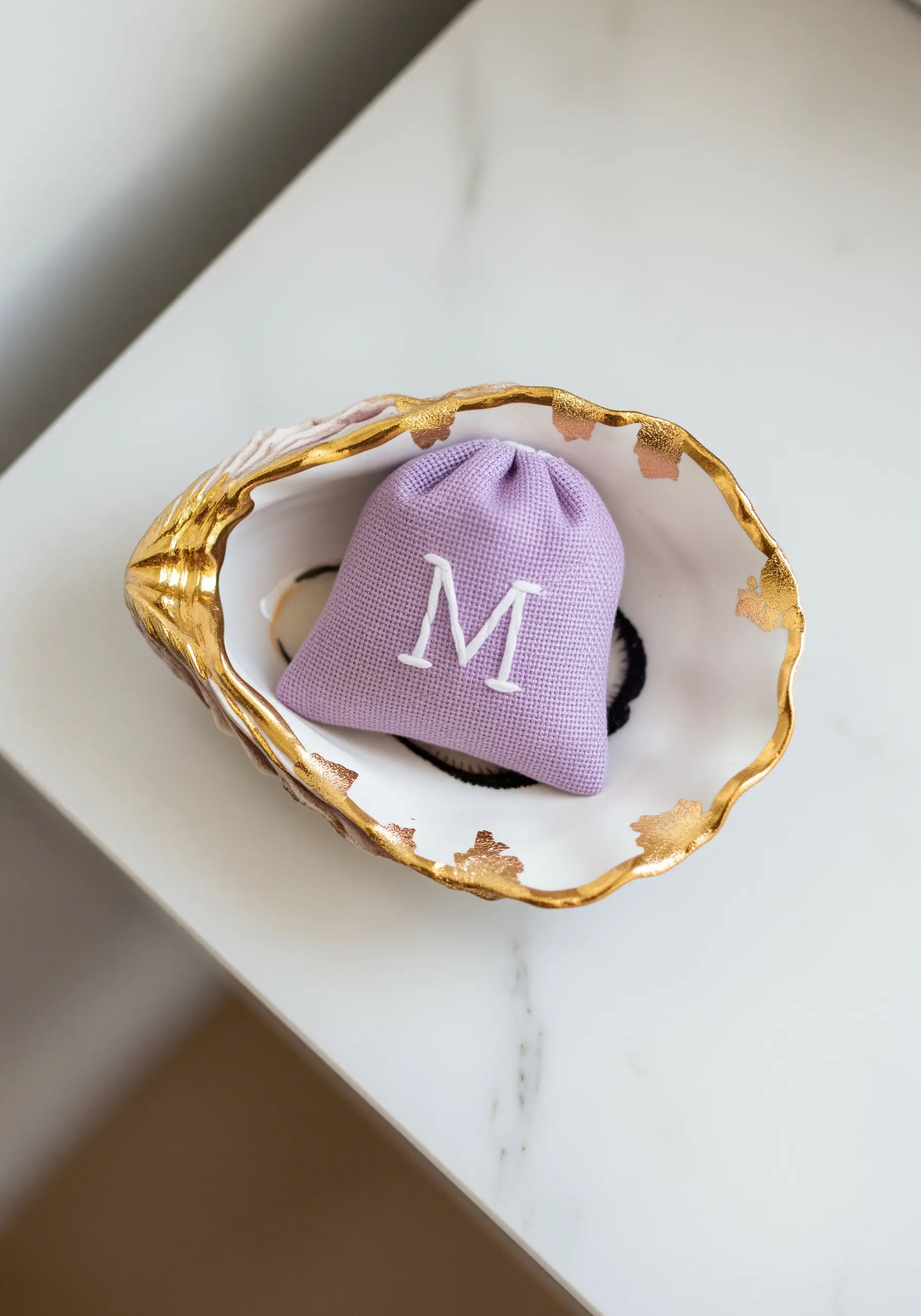 A crisp white embroidered 'M' monogram on a small lavender waffle-weave pouch.