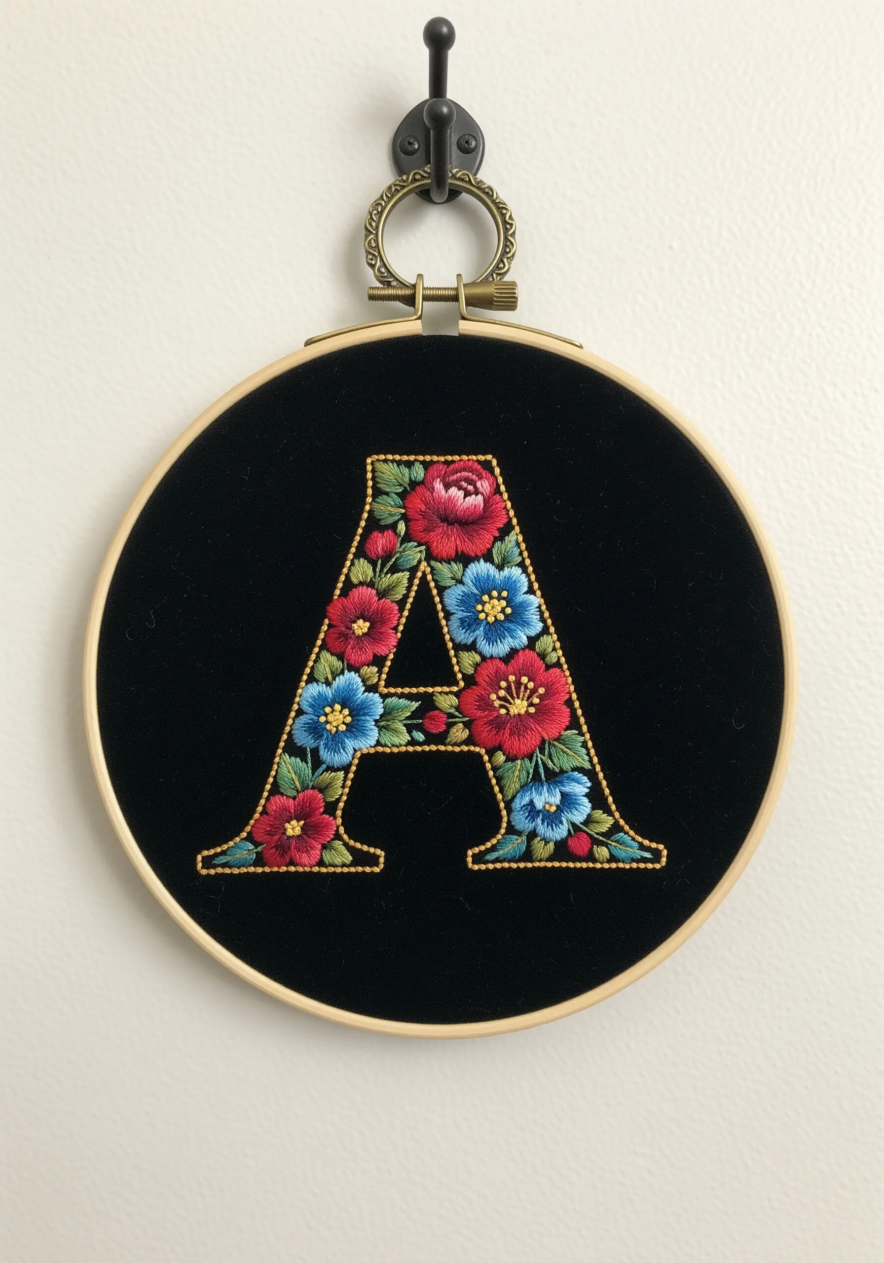 A floral-filled embroidered monogram 'A' on black velvet fabric in a hoop.