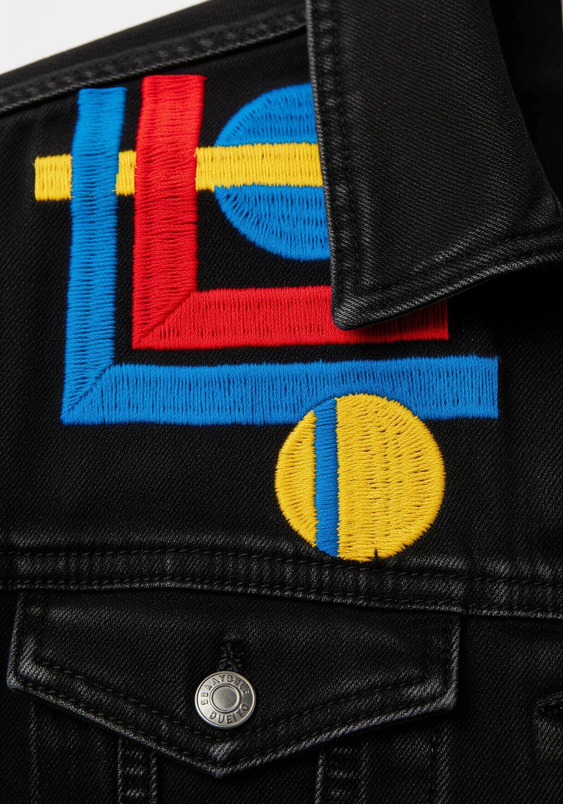 Abstract satin stitch design in primary colors on a black denim jacket collar.