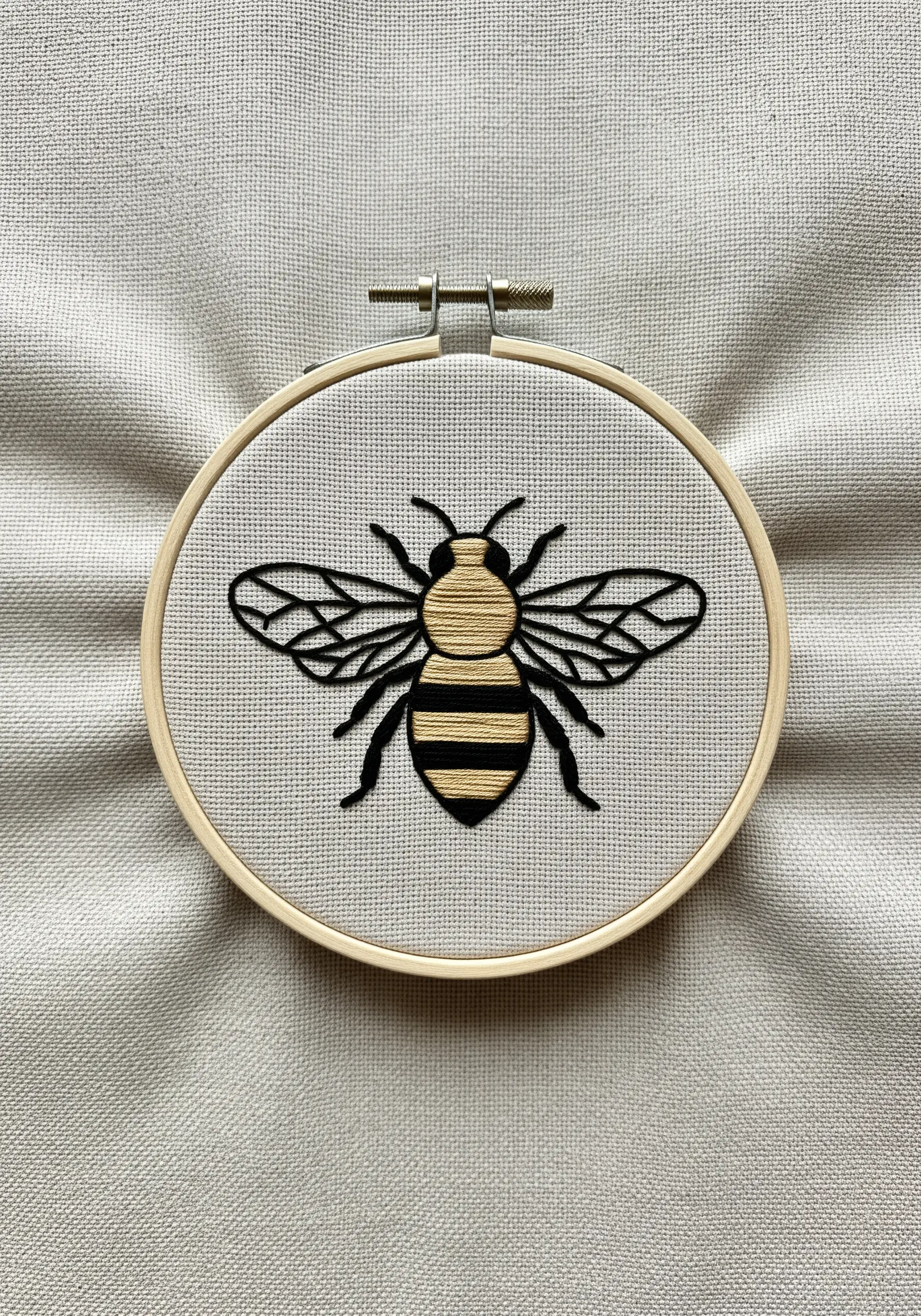 Close-up of a bee embroidery in a hoop with clean satin stitch and black outlines.