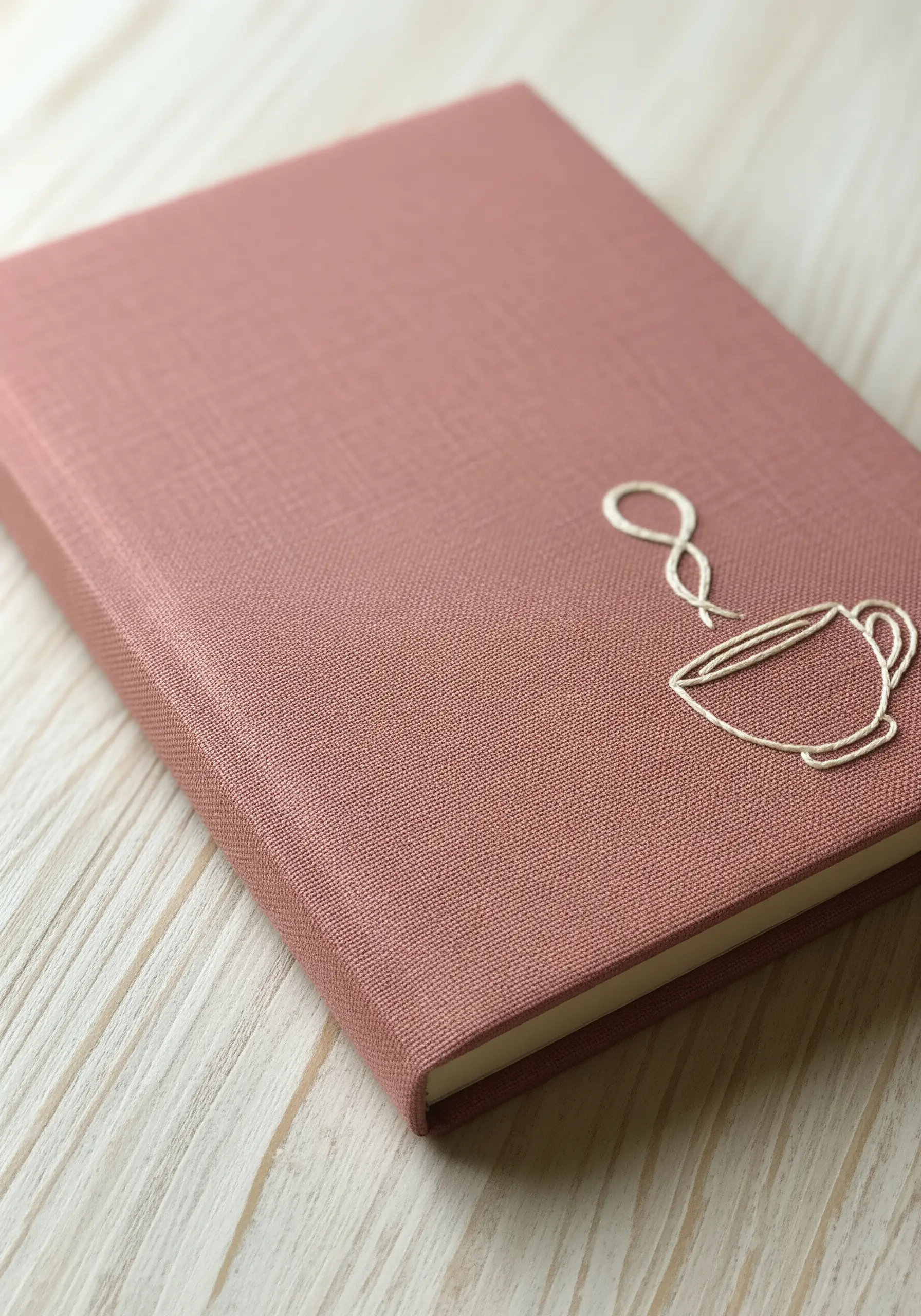 A simple line art embroidery of a coffee cup with steam, stitched in white thread.
