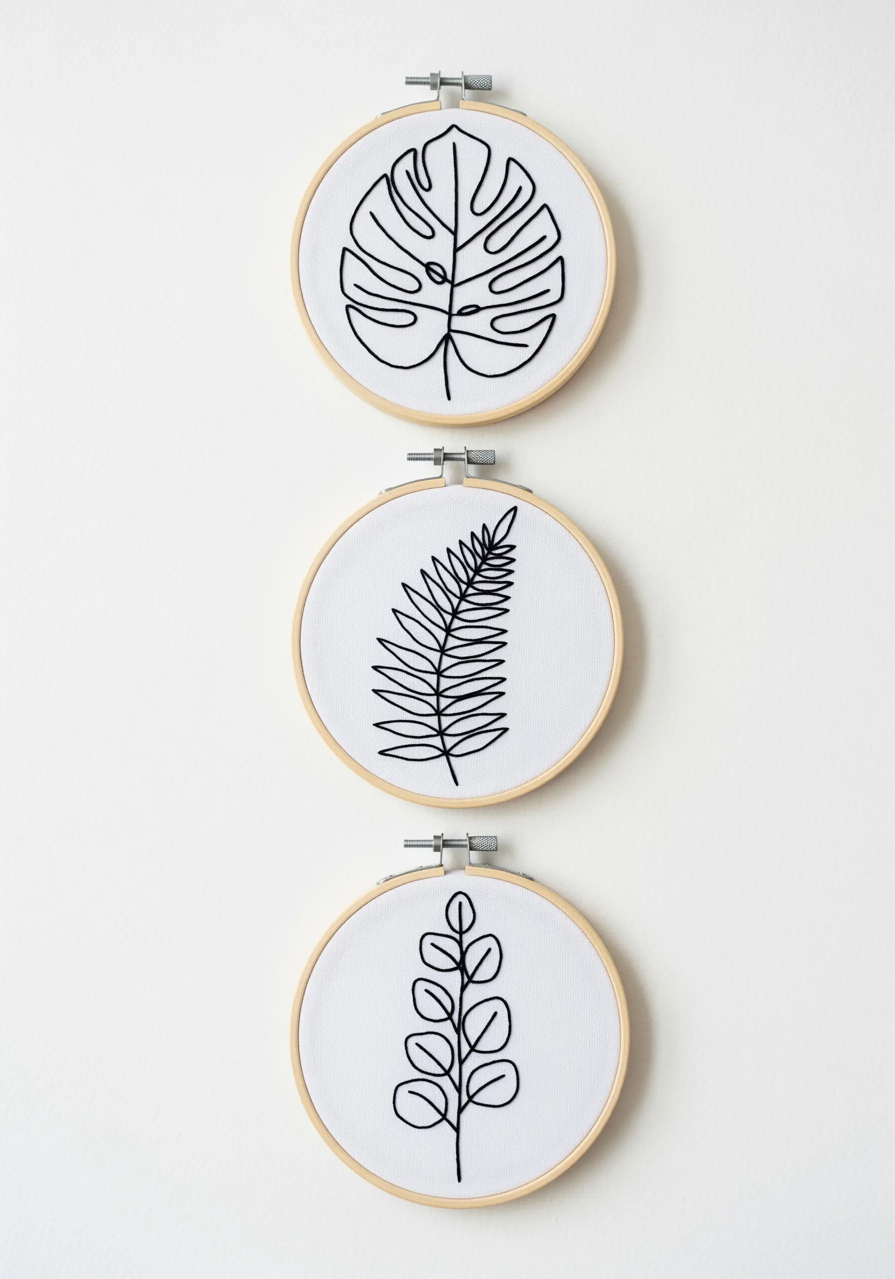 Three small embroidery hoops with minimalist black line art of different leaves.