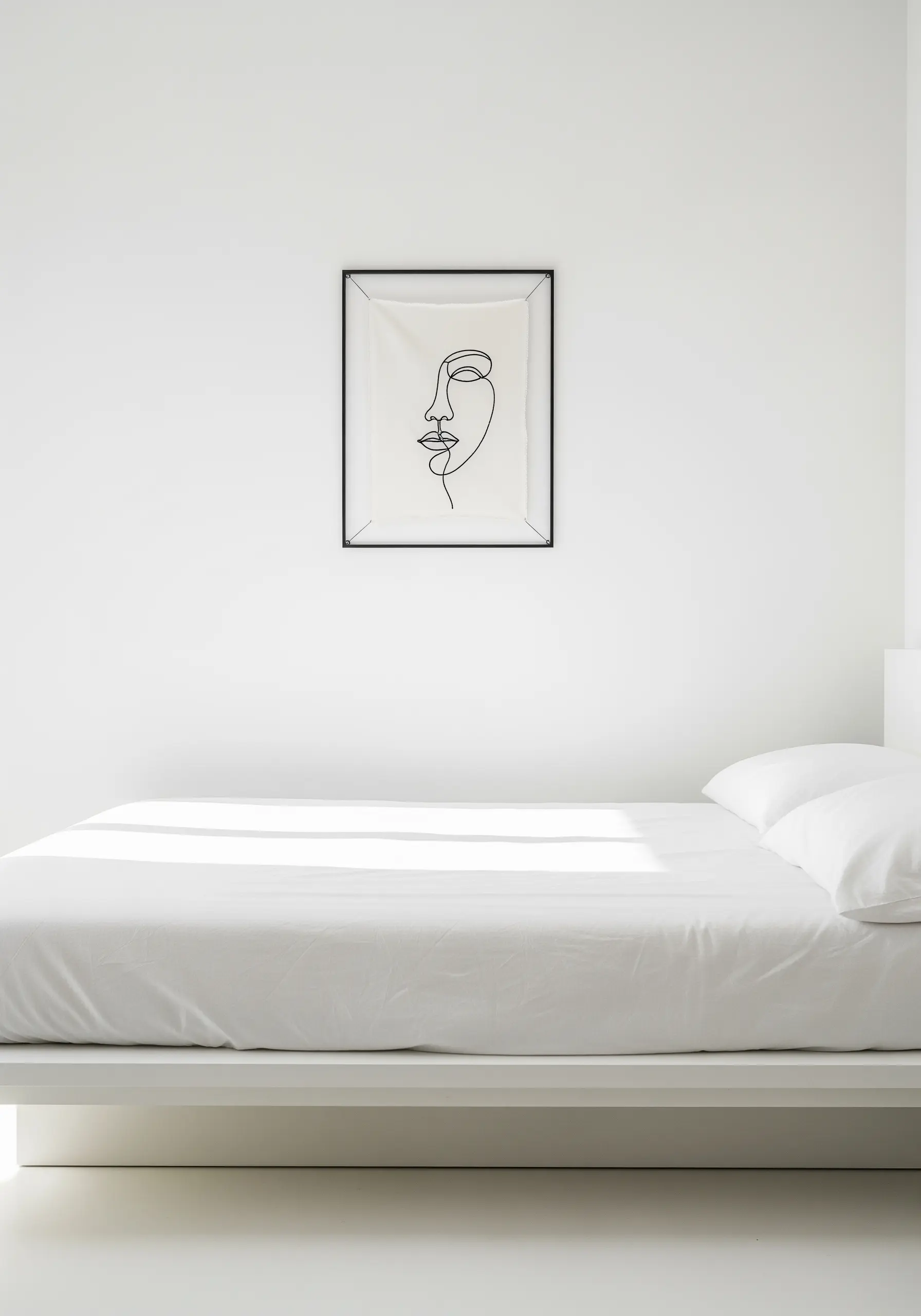 Minimalist single-line art embroidery of a face, framed and hung in a white bedroom.