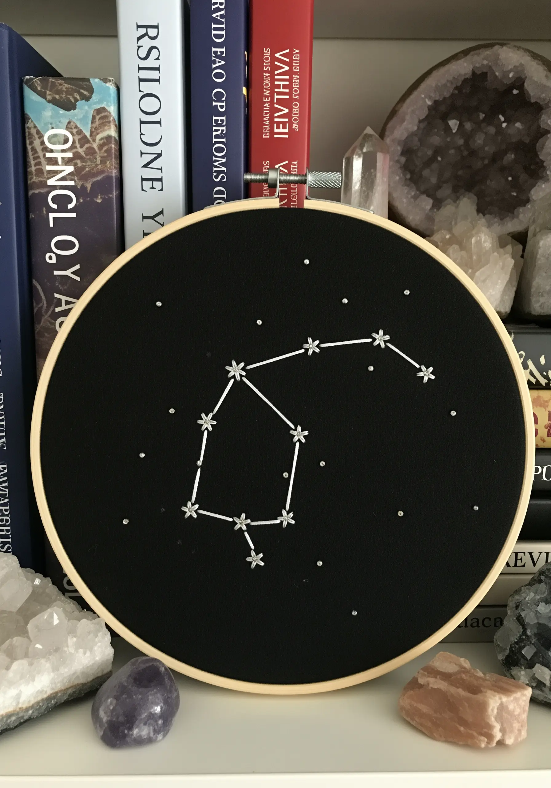An embroidered constellation on black fabric using white star stitches and lines.