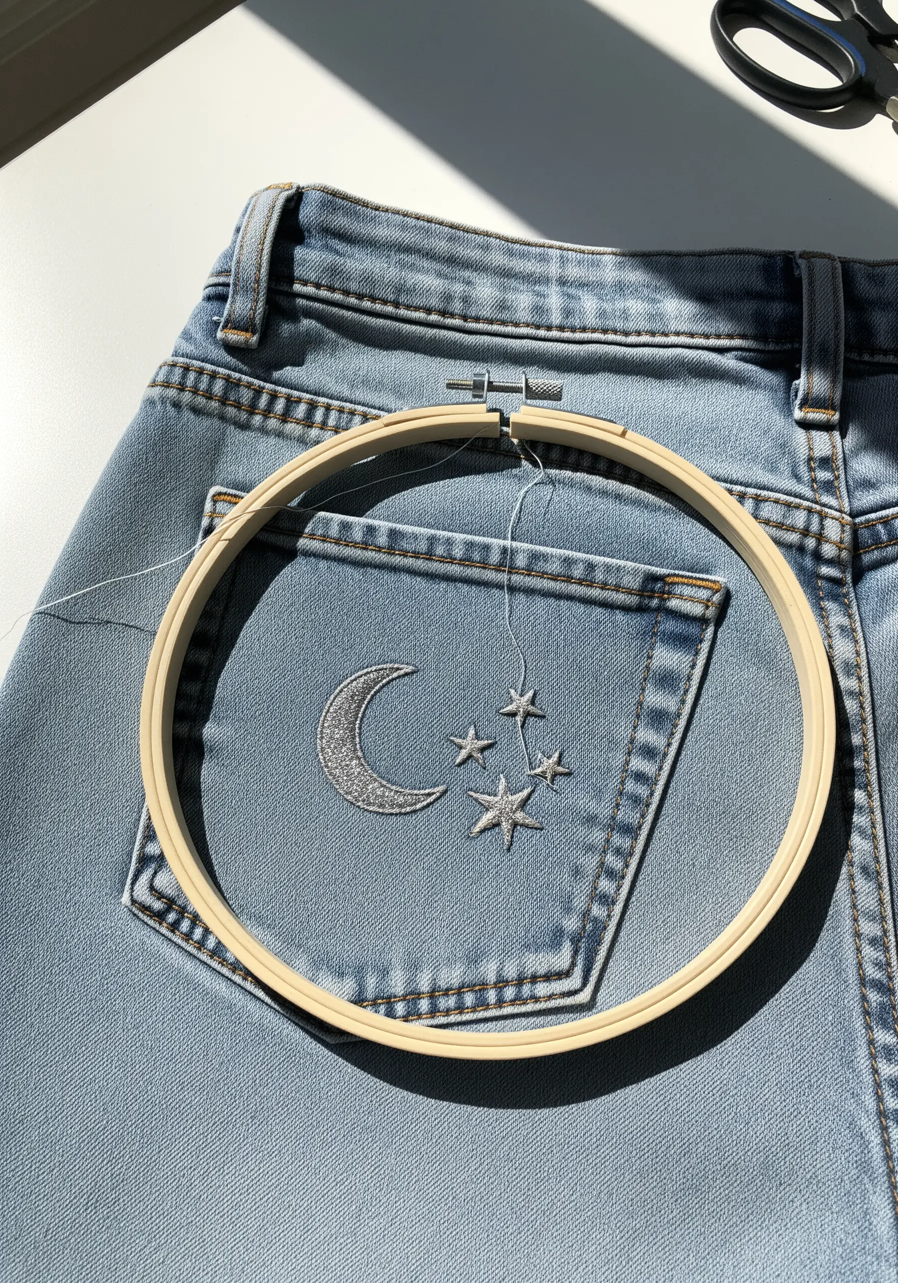 A silver metallic embroidered moon and stars on the back pocket of a pair of blue jeans.