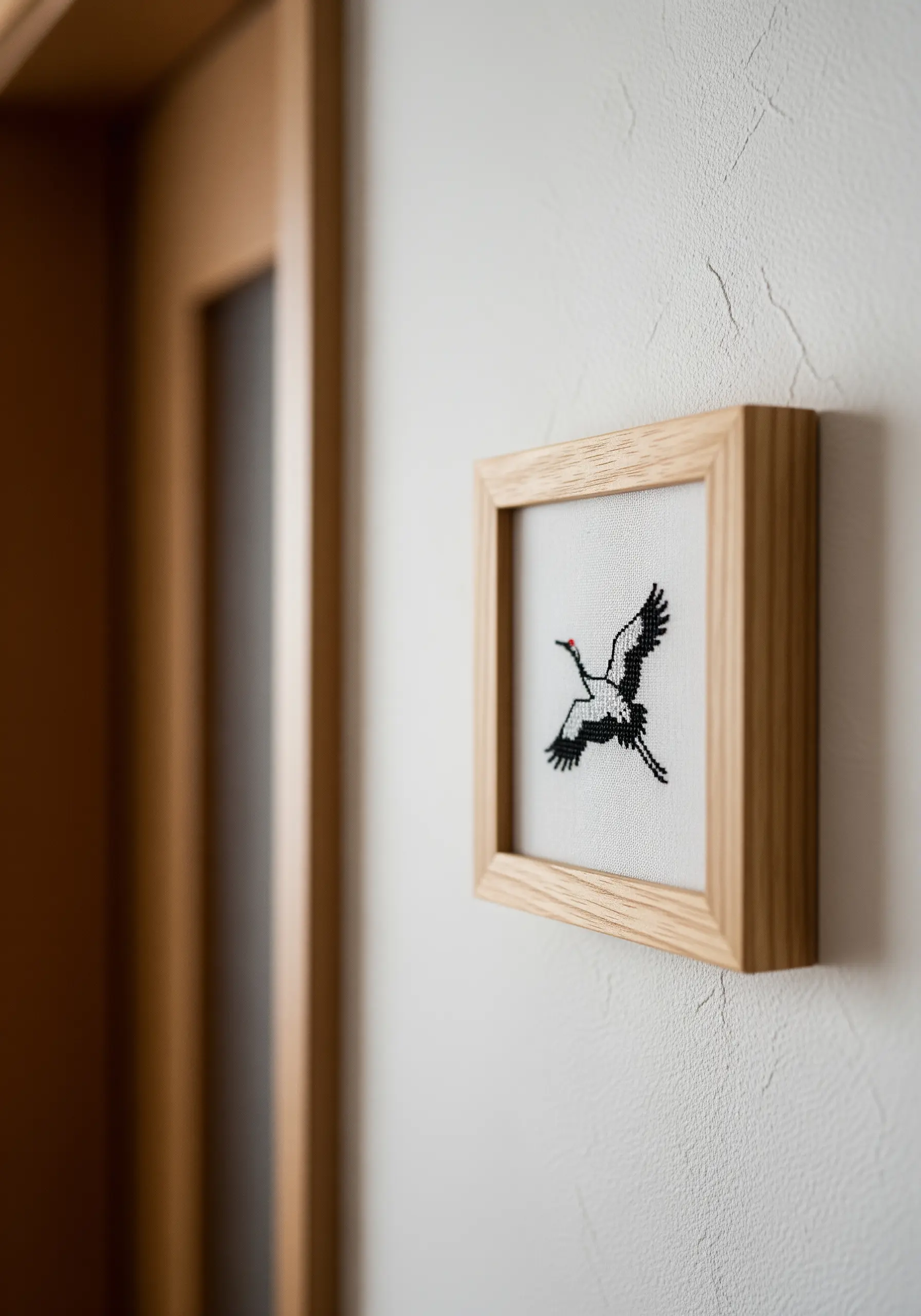 A tiny, framed cross-stitch of a black and white crane in flight.