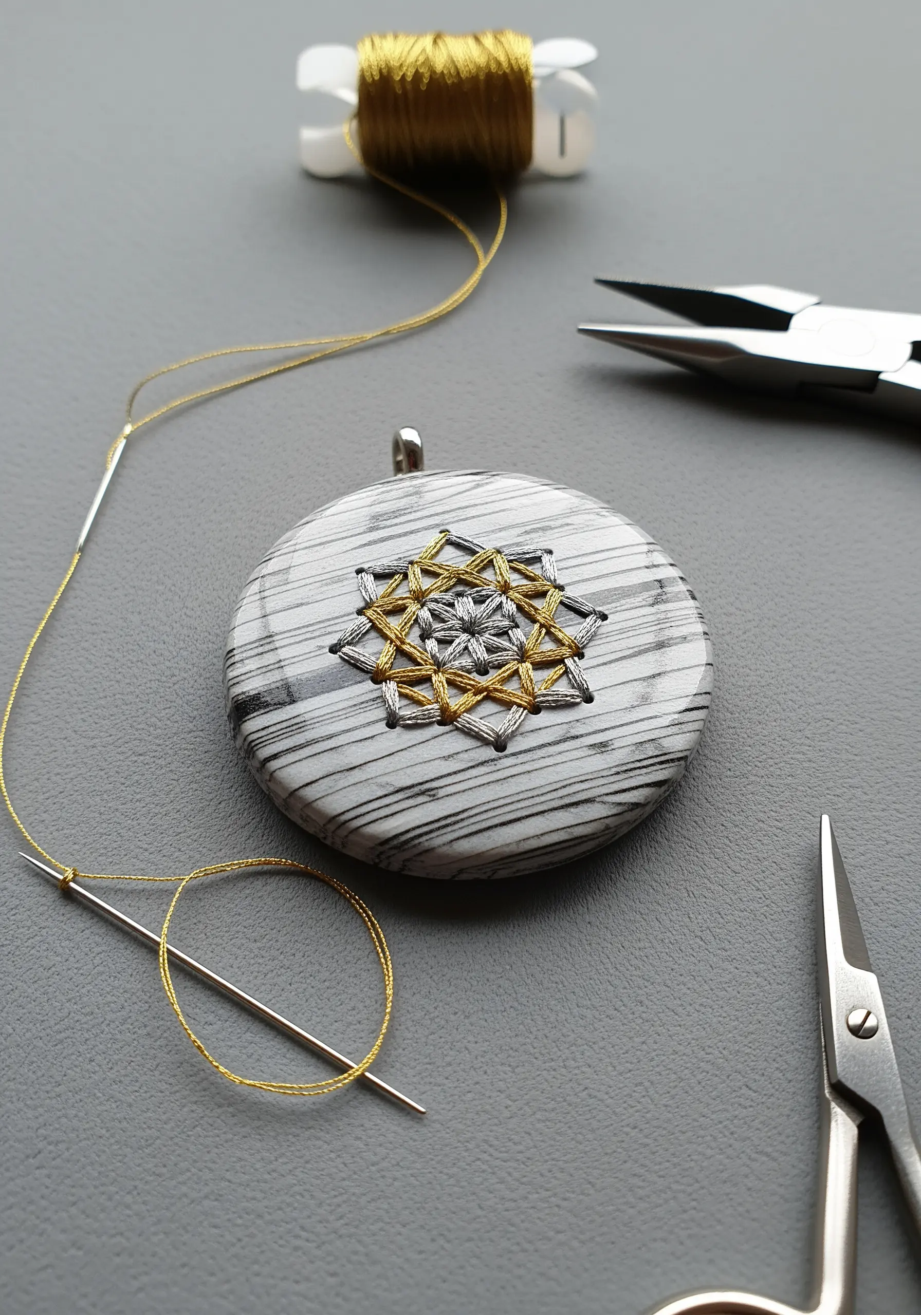 A geometric pattern stitched with gold and silver thread onto a drilled marble-patterned stone.