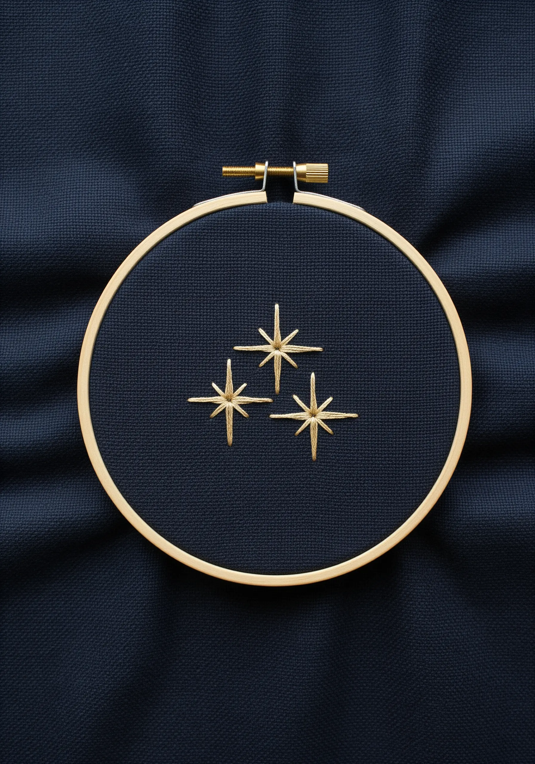 Three gold starbursts stitched with straight stitches on dark navy fabric.