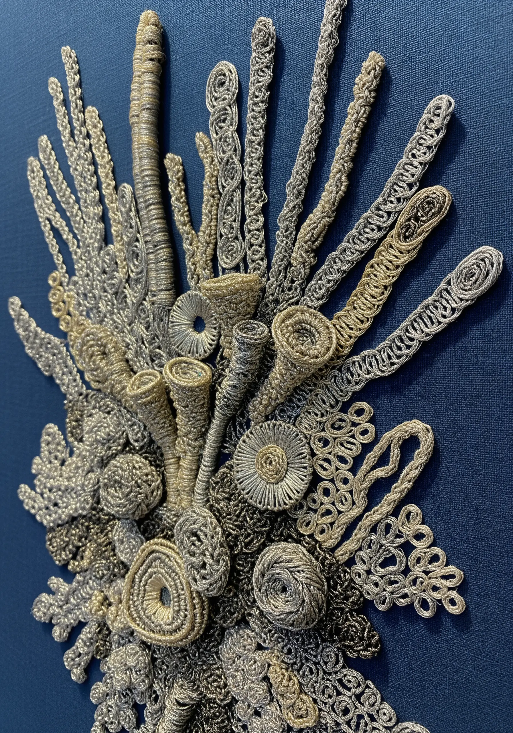 A sculptural arrangement of dimensional metallic stitches mimicking coral on a blue background.