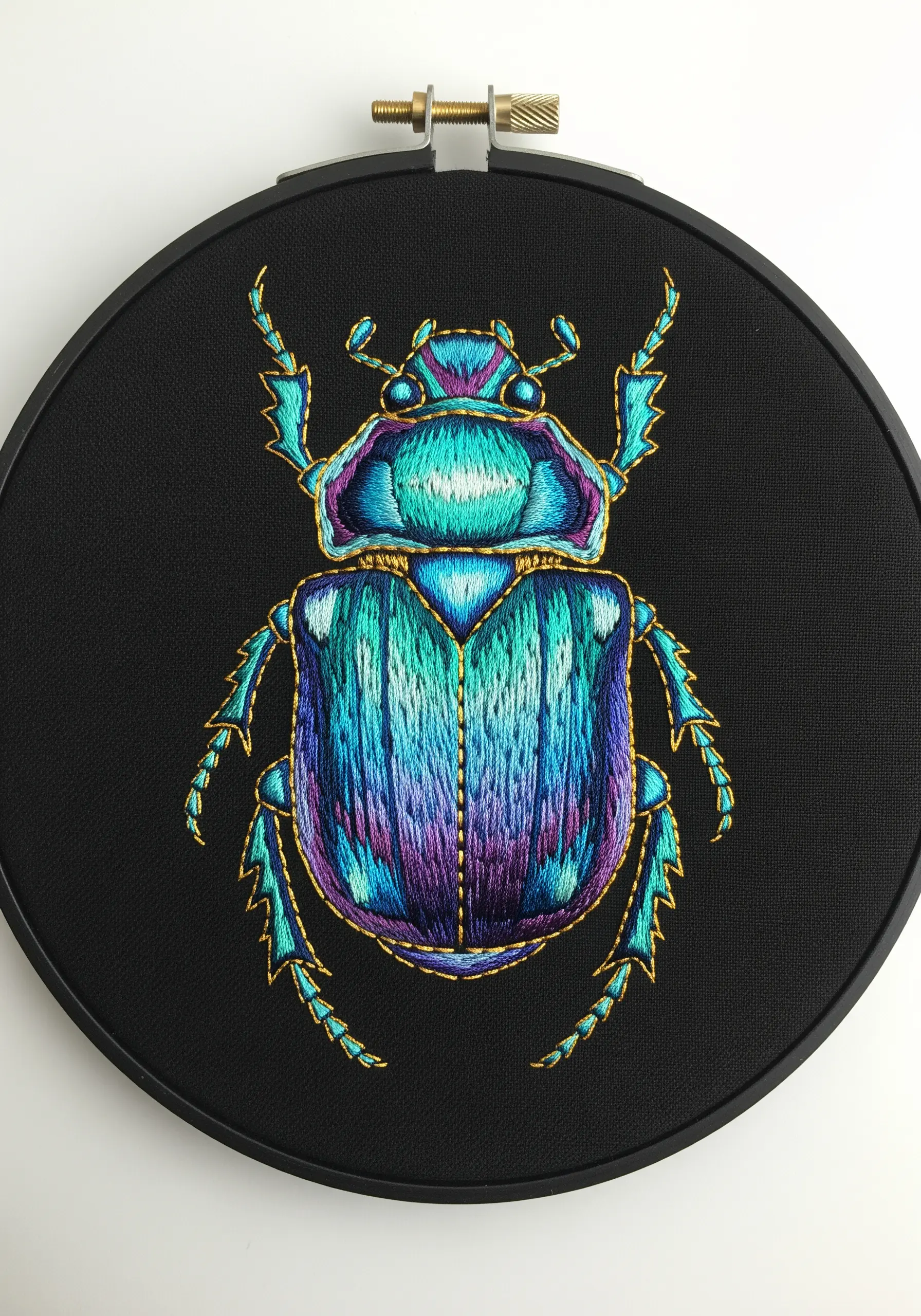 An iridescent beetle embroidered with vibrant blue, purple, and green threads on black fabric.