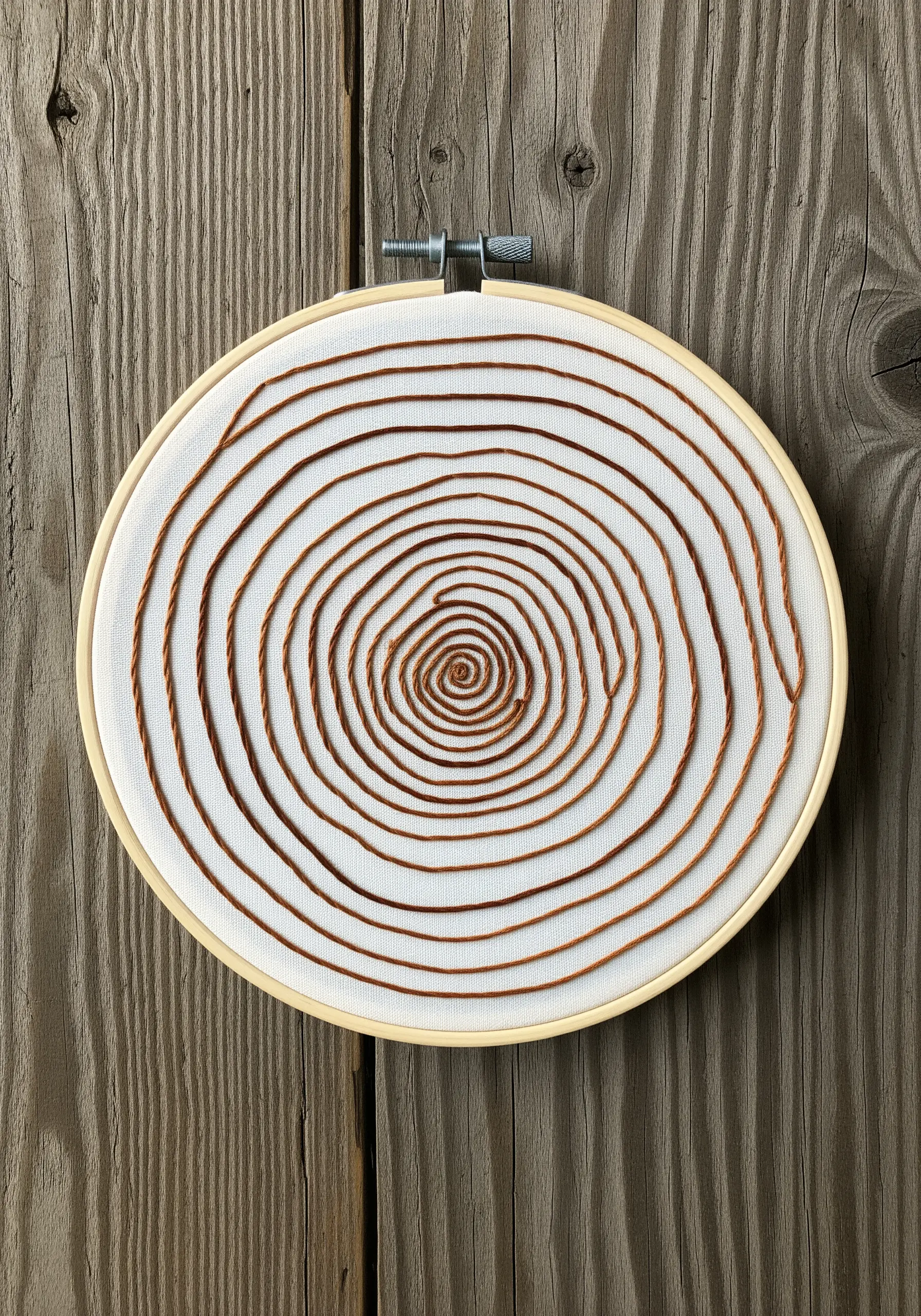 Concentric tree rings embroidered with a thick, couched brown thread on white fabric.
