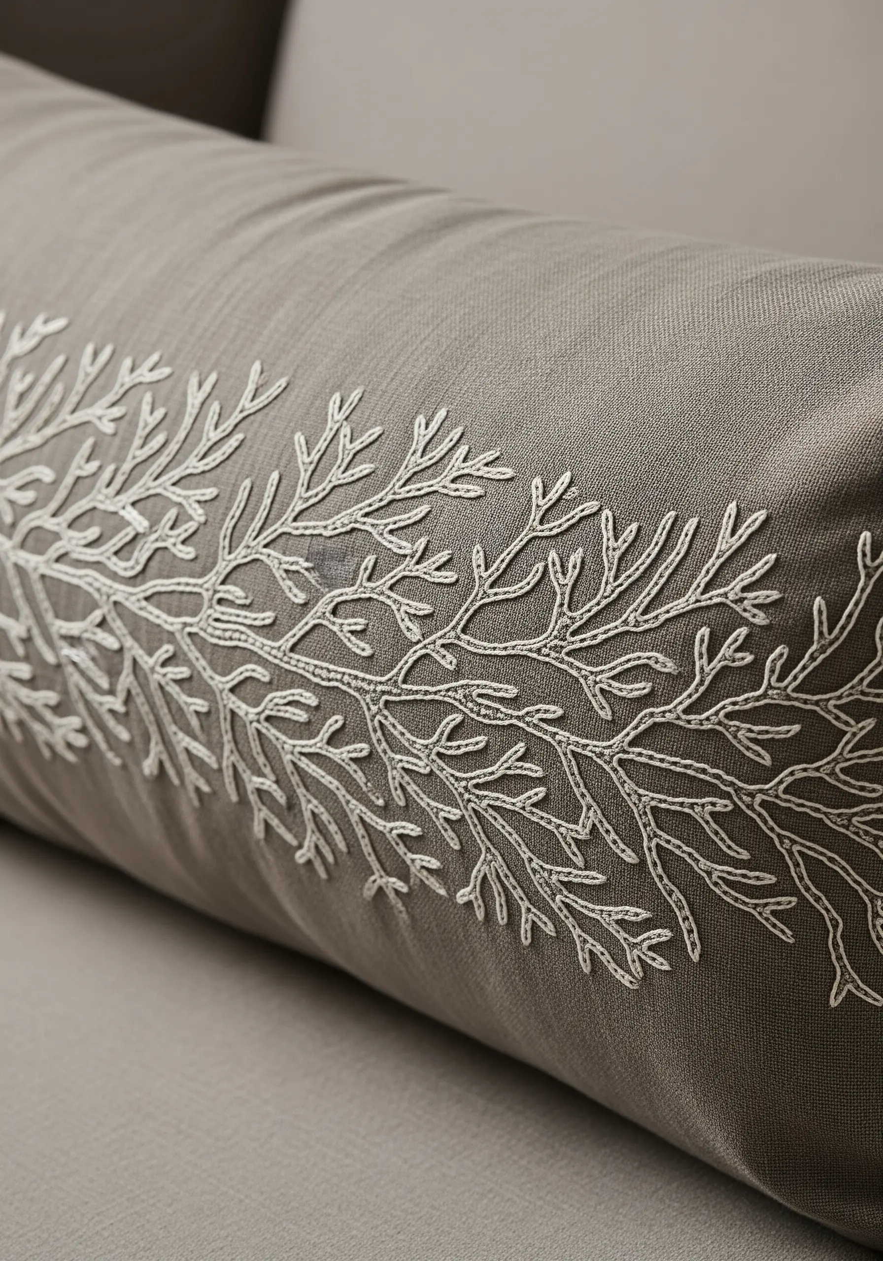 Intricate white embroidery of a coral branch spreading across a grey lumbar pillow.