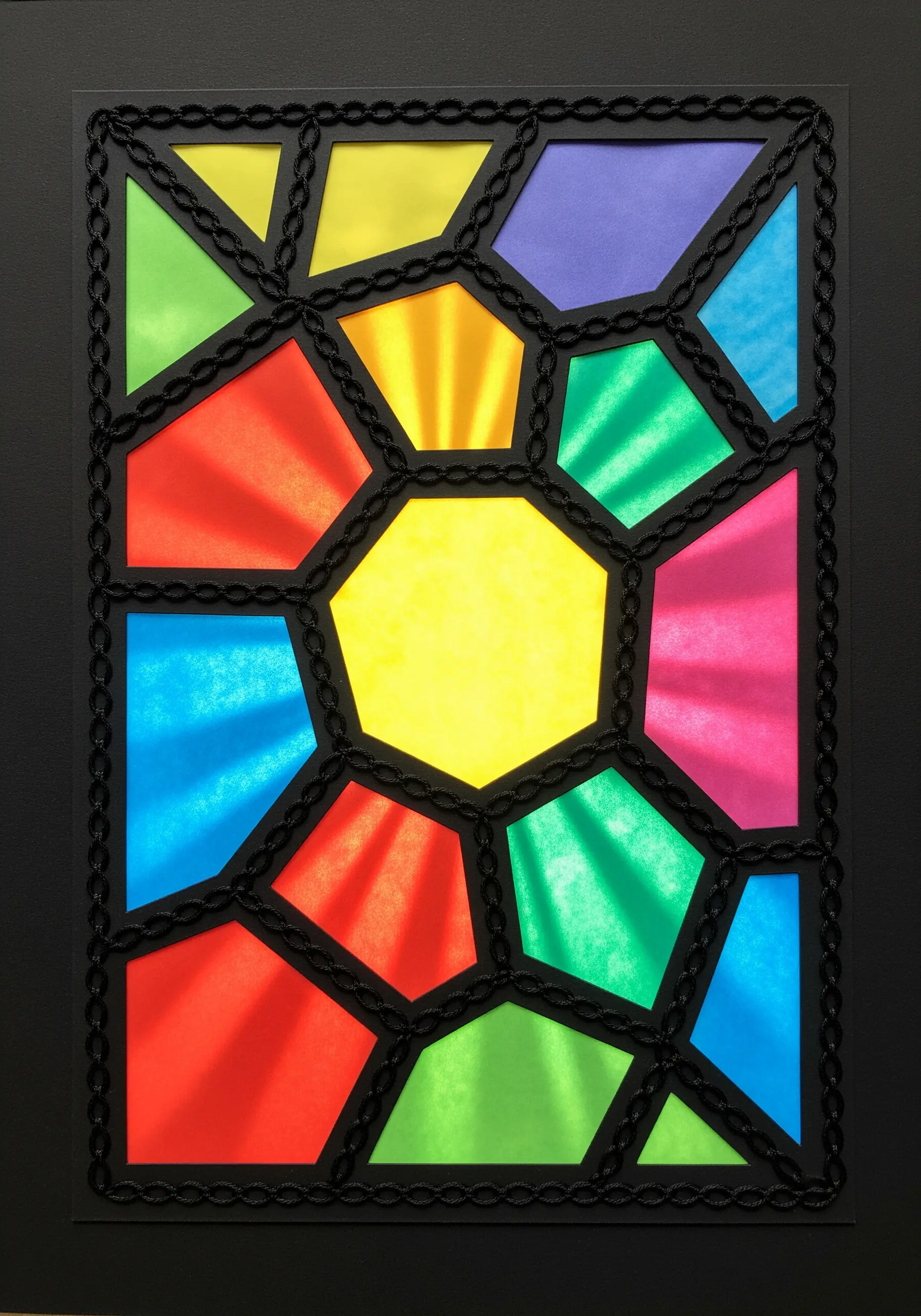A stained glass window design made with colorful paper and bold, black chain stitch embroidery outlines.