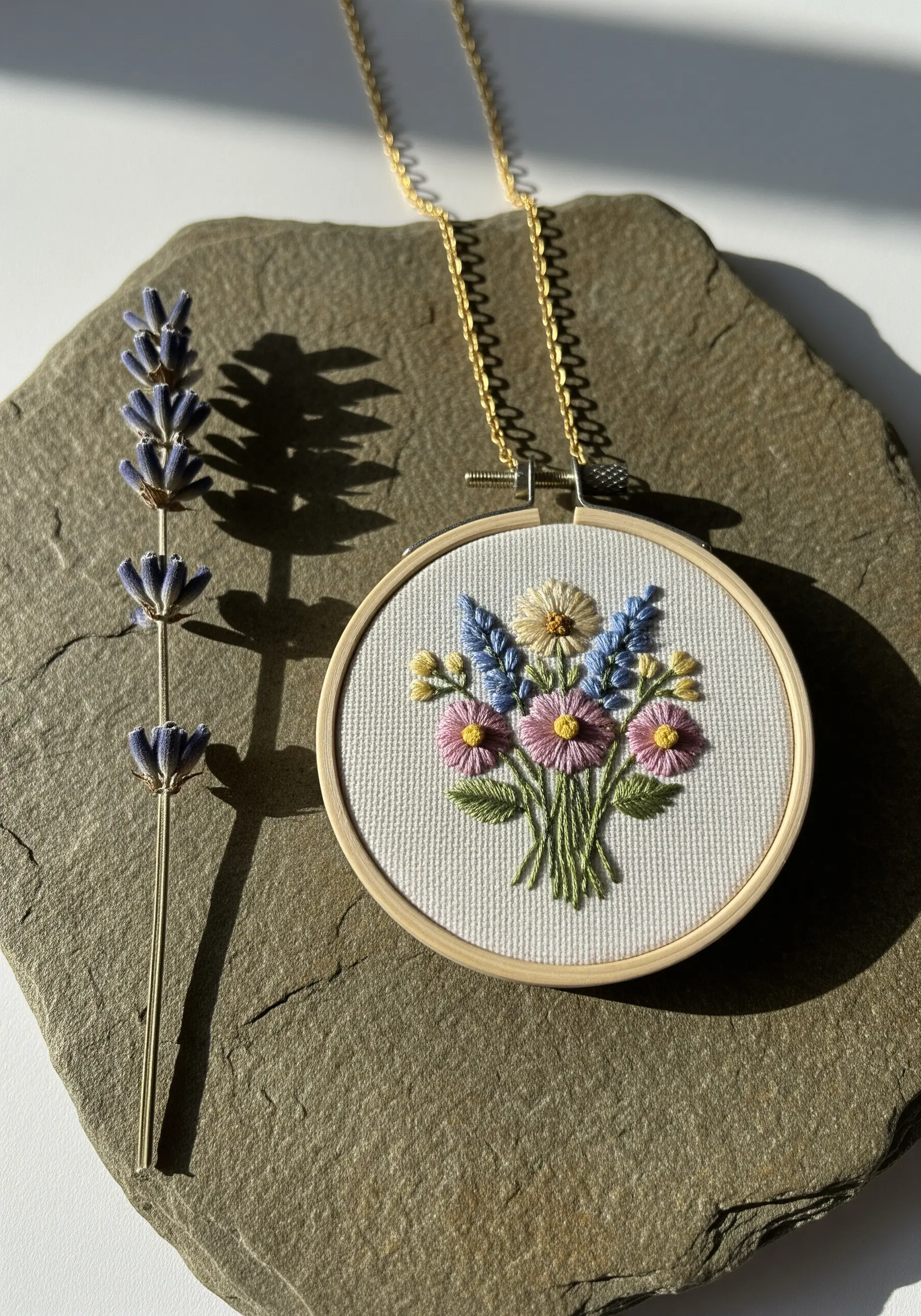 Miniature embroidered floral bouquet with French knots and detached chain stitches in a small hoop necklace.