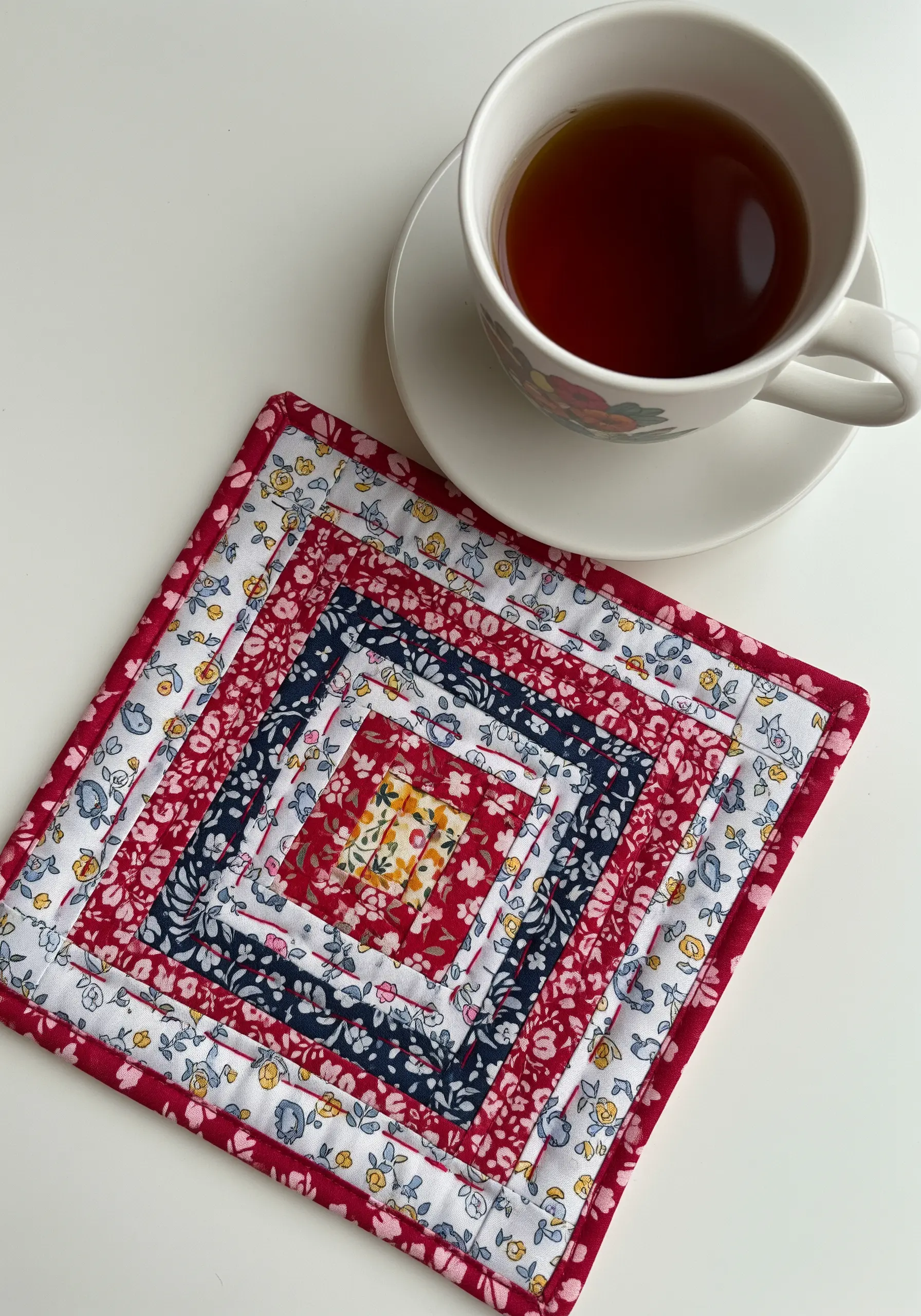 A quilted coaster made from floral and solid fabric strips in a log cabin pattern.