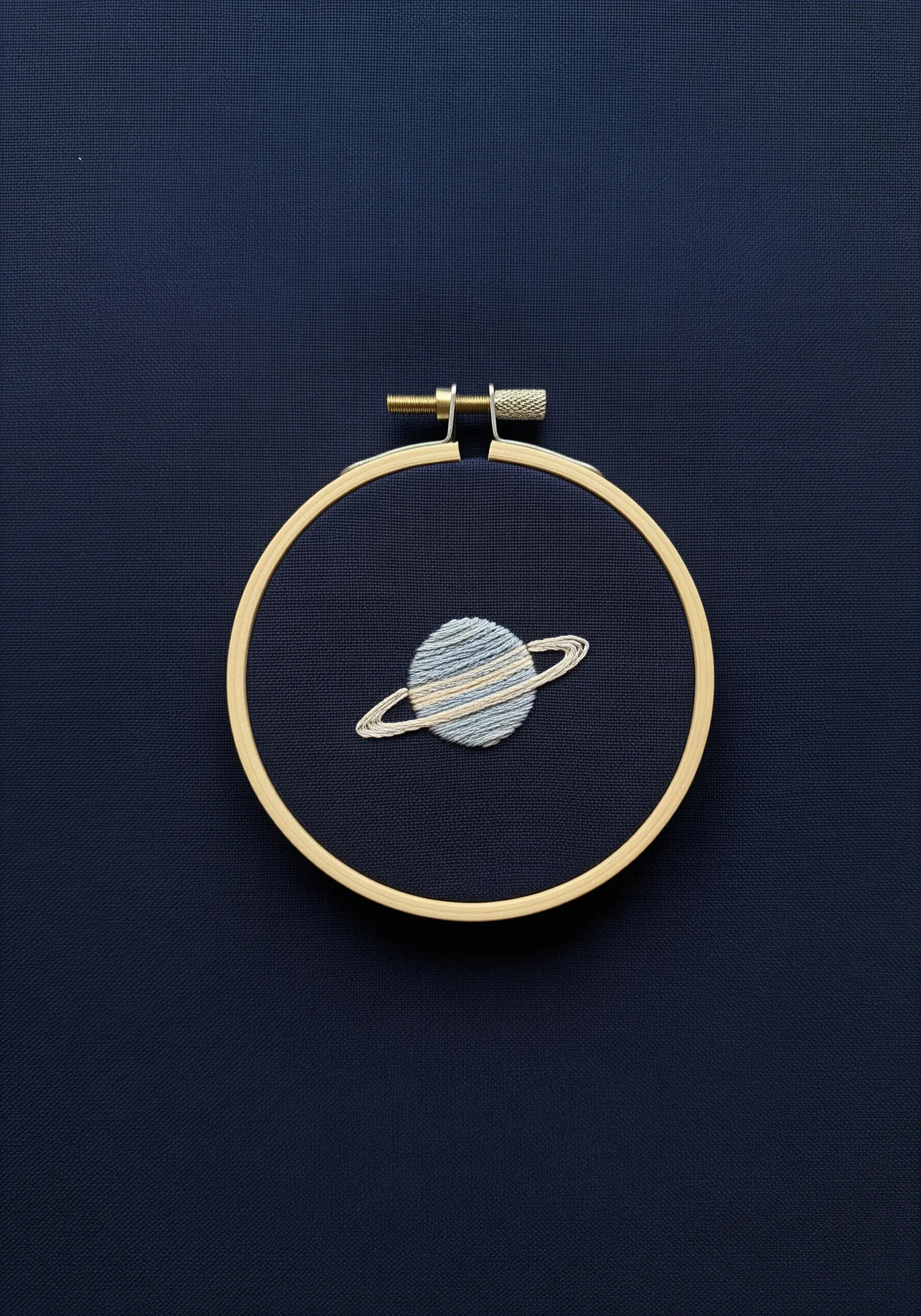 A tiny planet Saturn with blue, grey, and white satin stitches on navy fabric.