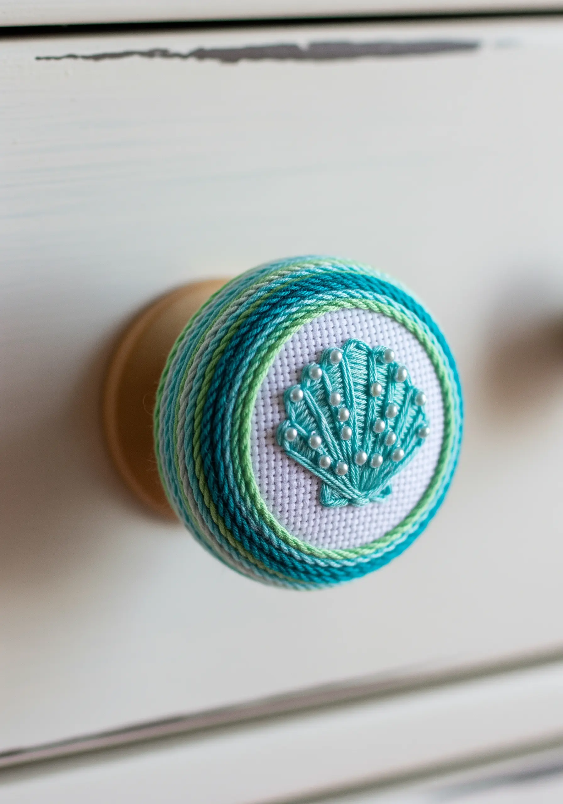 A drawer knob decorated with wrapped thread and an embroidered seashell with pearls.