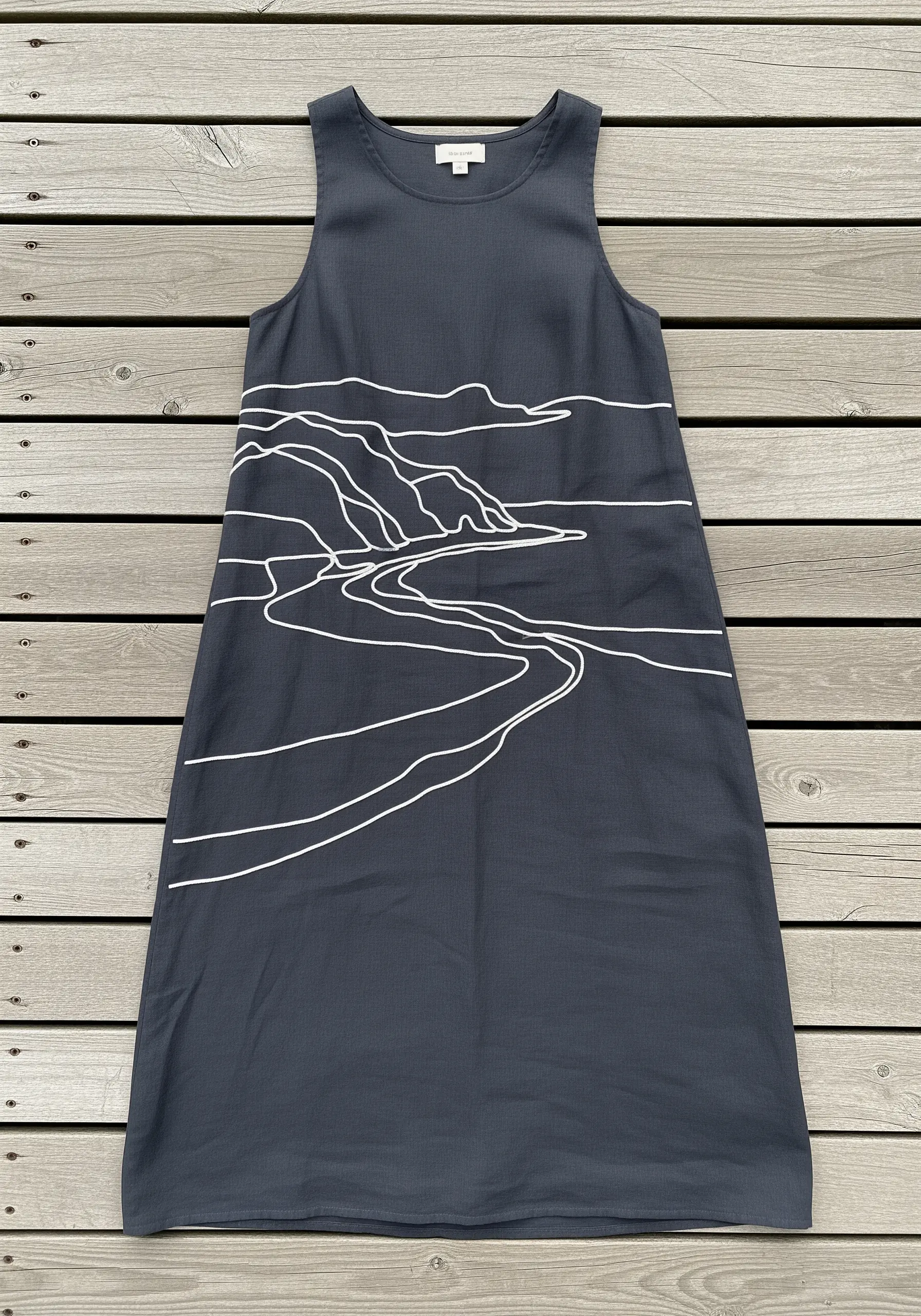 A minimalist white line art embroidery of a coastal landscape on a dark gray shift dress.
