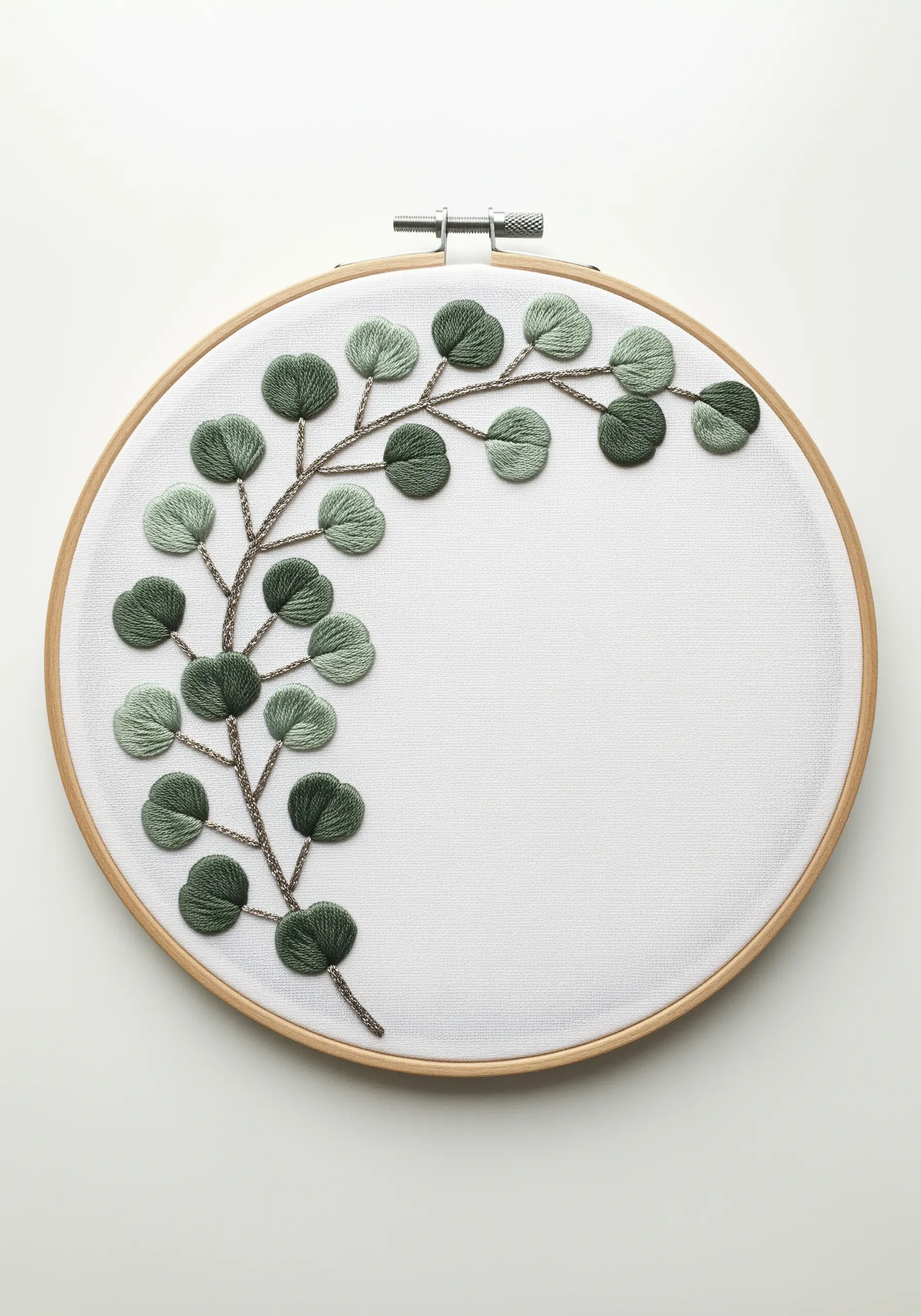 A single branch of eucalyptus with green satin-stitched leaves on a white fabric background.