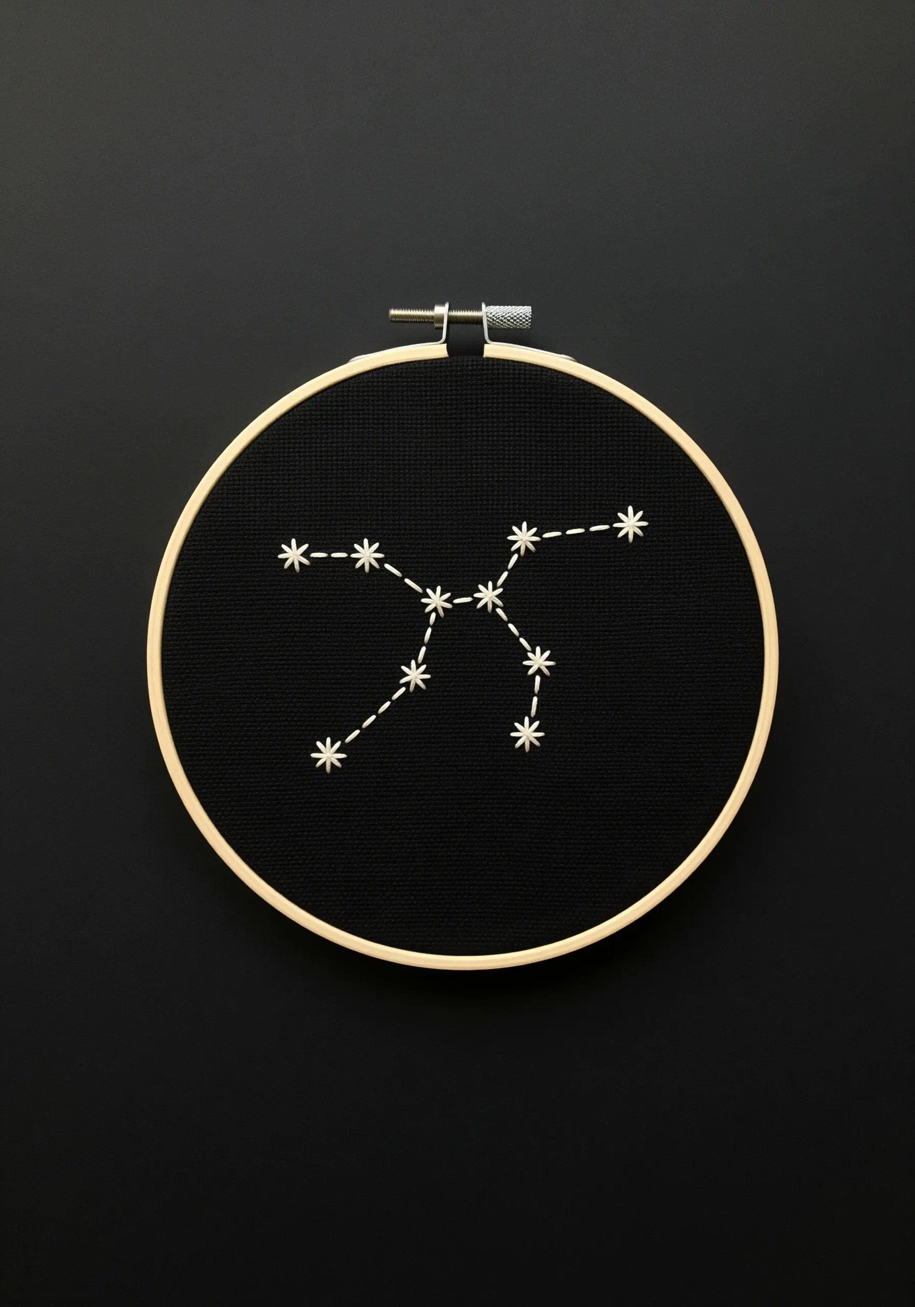 A white constellation stitched on black Aida cloth inside a wooden hoop.
